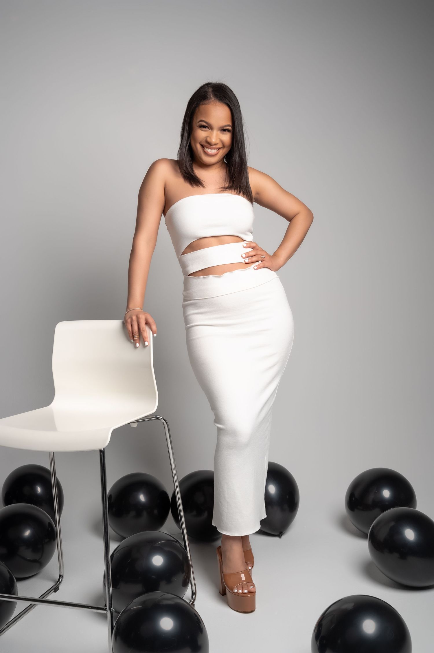 Modern fashion shoot with white outfit and black balloons in minimalist studio setting.