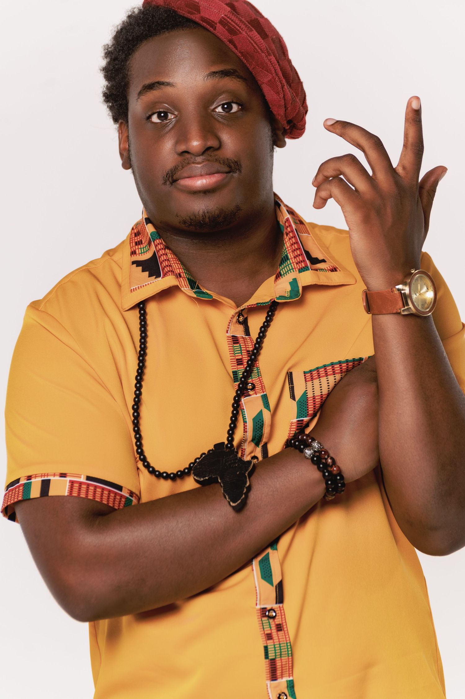 Expressive poses in yellow polo shirt with African-inspired accessories and red headwrap.