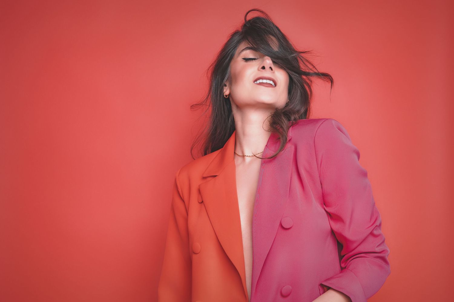 A person wearing a split-colored red and pink blazer poses joyfully against a red background.