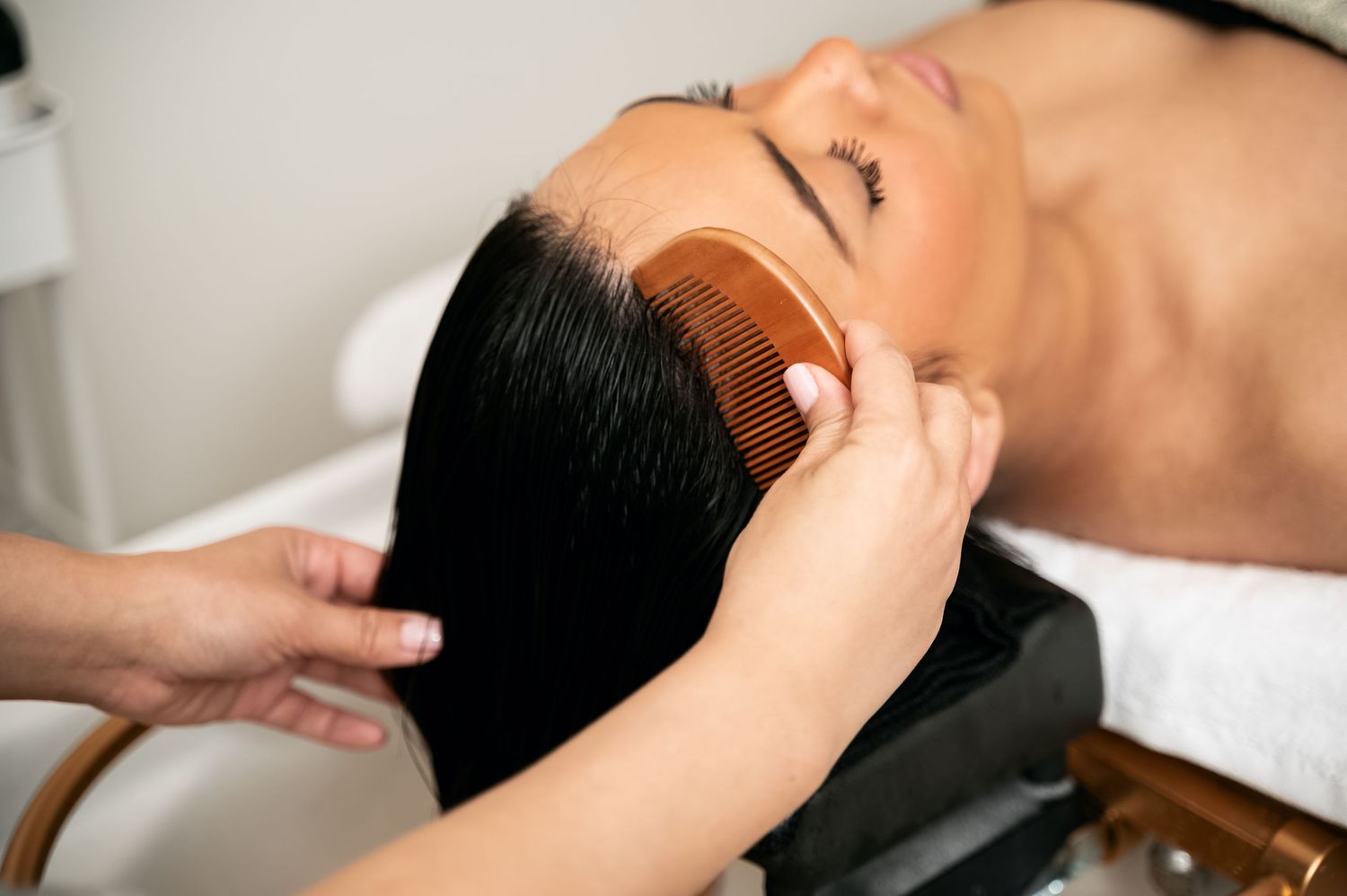 Massage therapist performs gentle neck and head massage techniques on a client lying on treatment table.