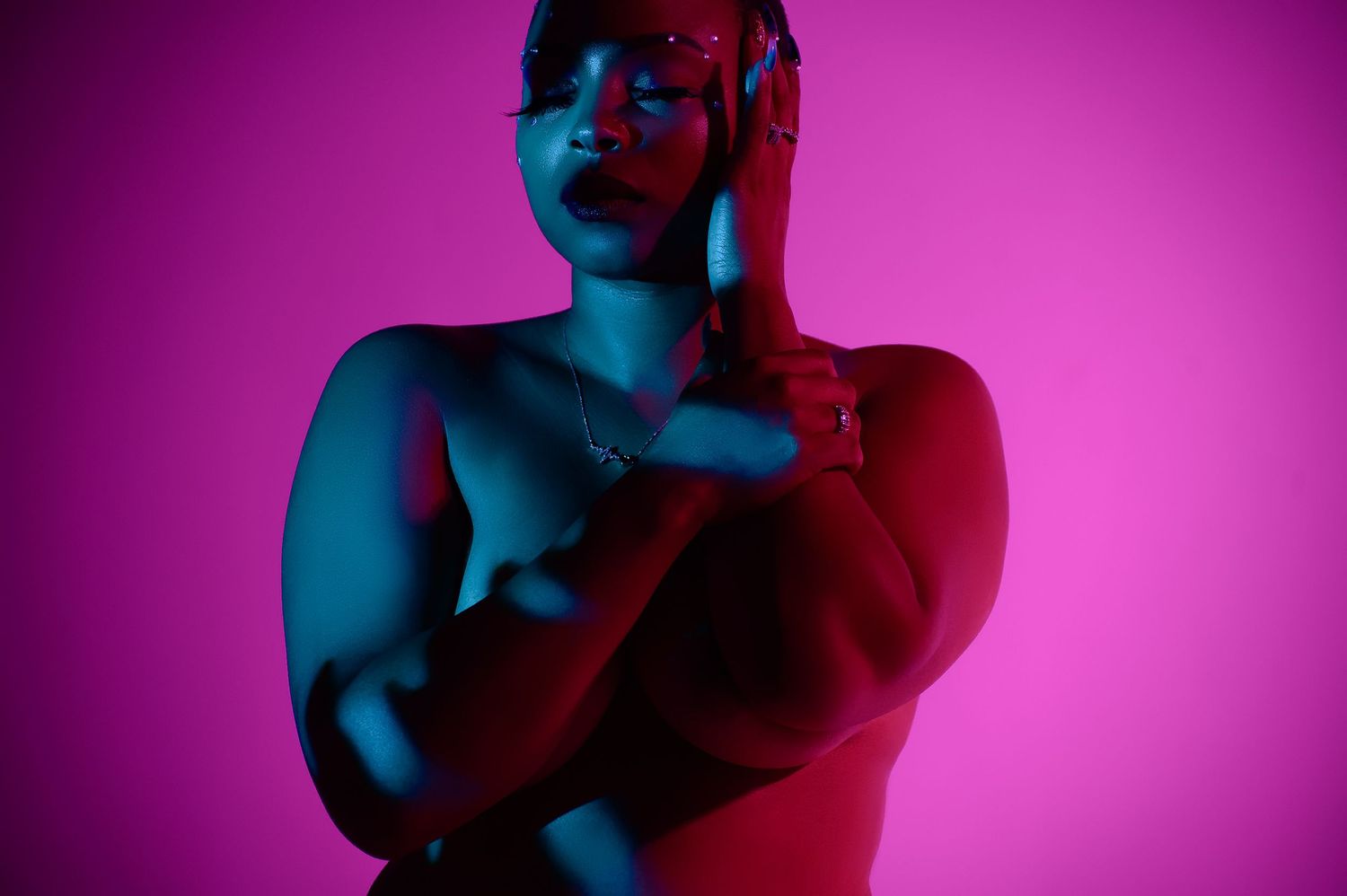 Person posing under dramatic blue and red neon lighting on pink background.