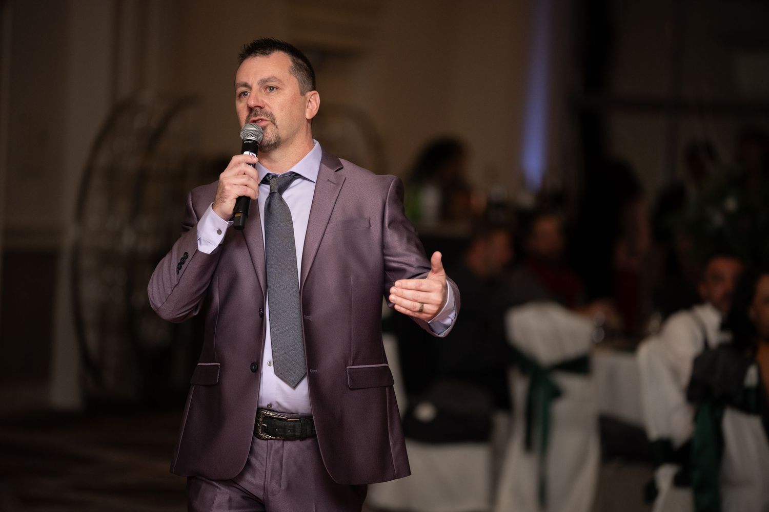 Speaker gesturing while delivering presentation in formal attire at evening event.