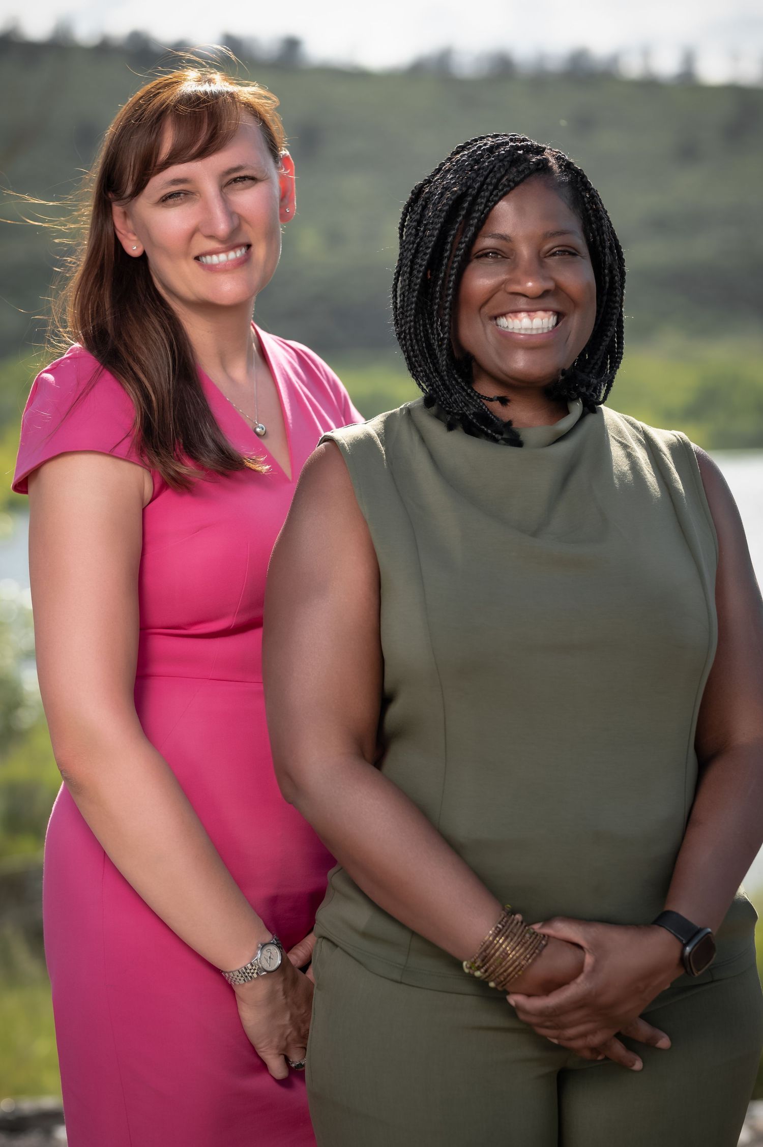 Two friends in pink and olive green outfits pose together outdoors while smiling at the camera.