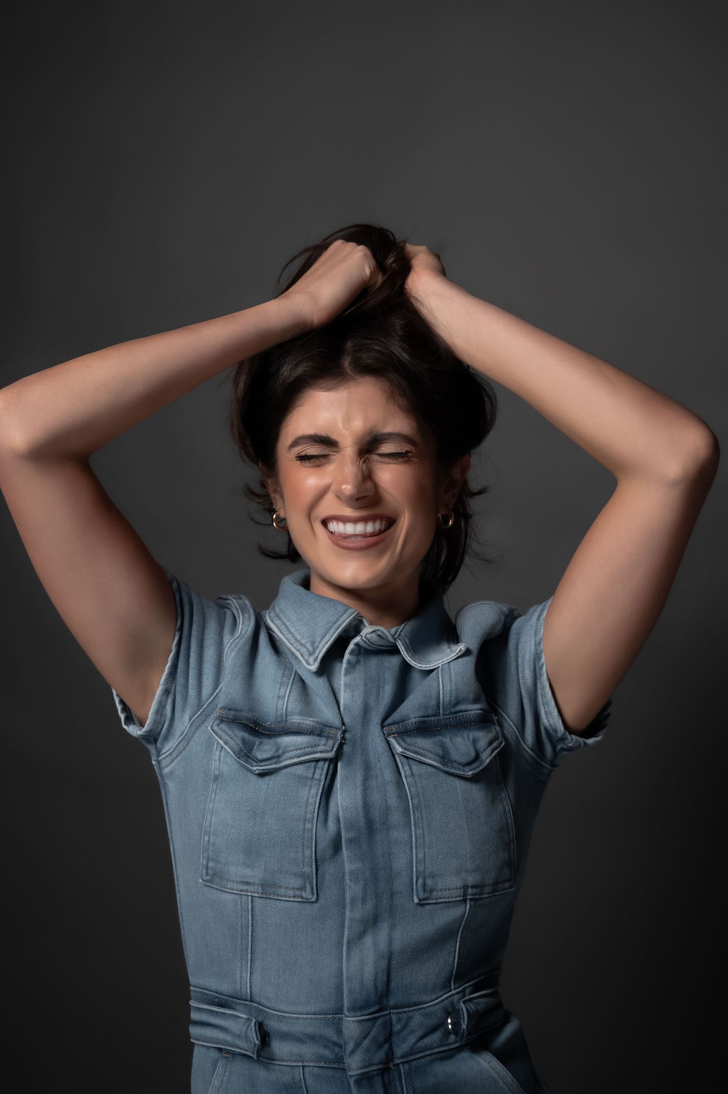 A joyful expression of emotion in a denim shirt against a dark background.
