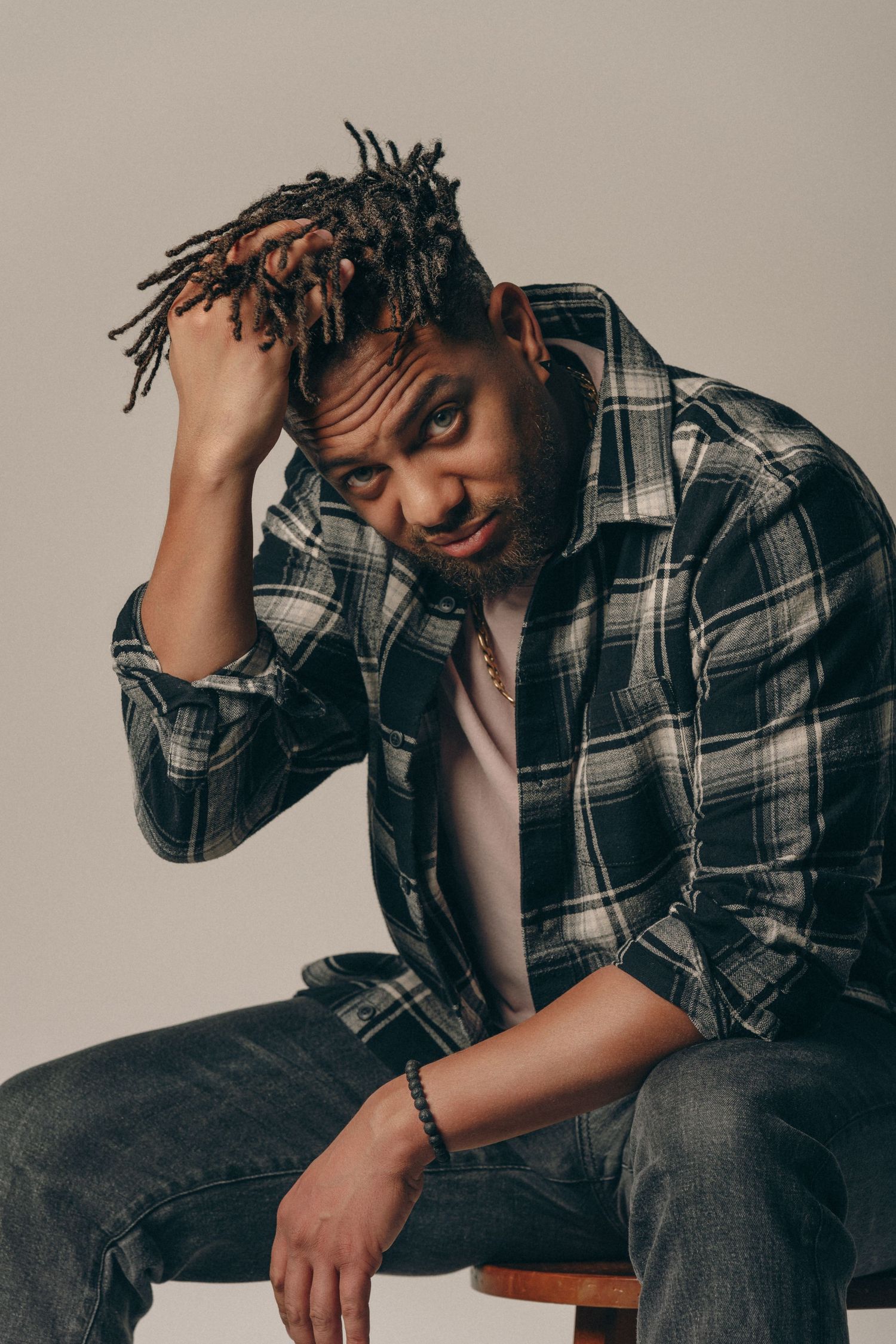 Stylish portrait series showing person in plaid shirt posing casually on wooden stool against neutral background.