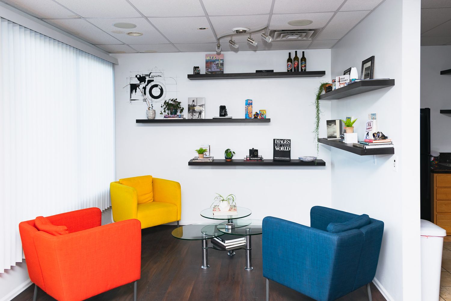 Modern office lounge area with colorful cube seating and floating wall shelves displaying various decorative items.