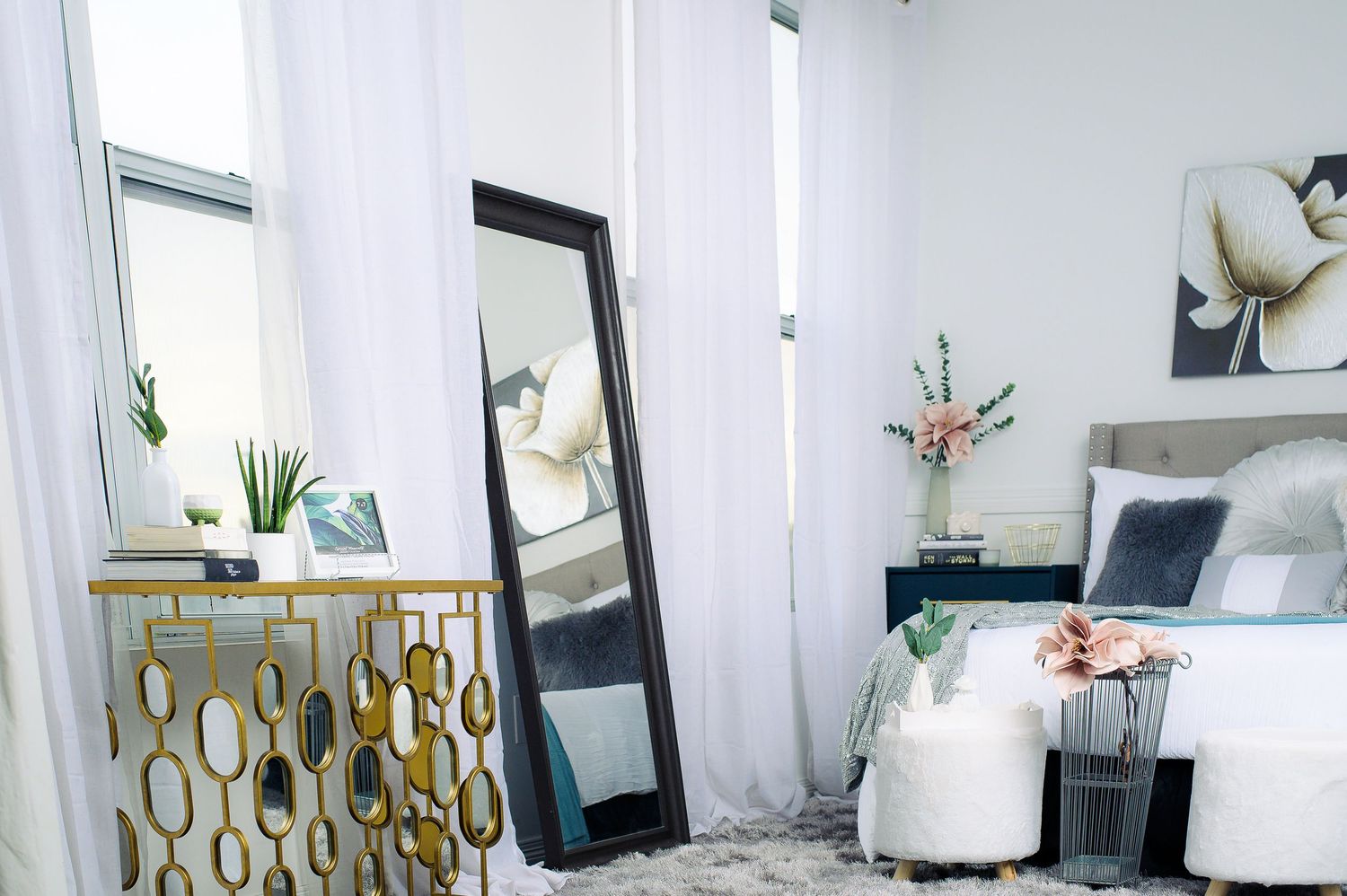 Modern white living room with gold accents features a plush sofa, decorative mirrors, and potted plants.