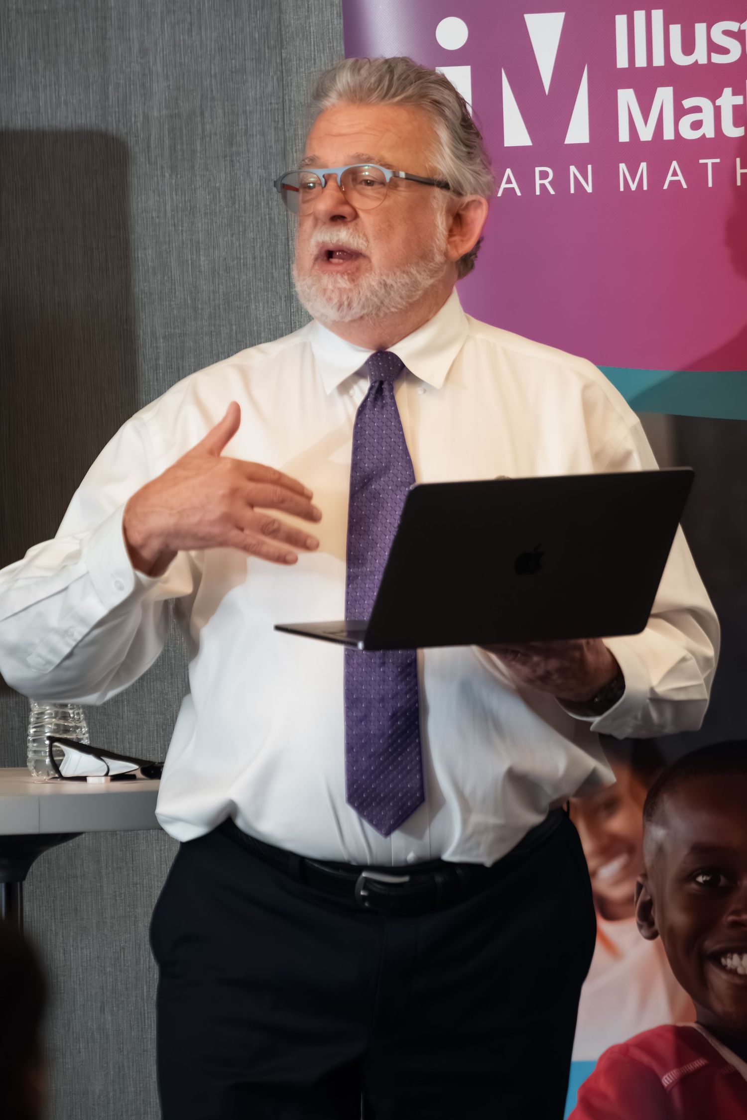 Professional speaker giving animated presentation in front of purple branded backdrop.