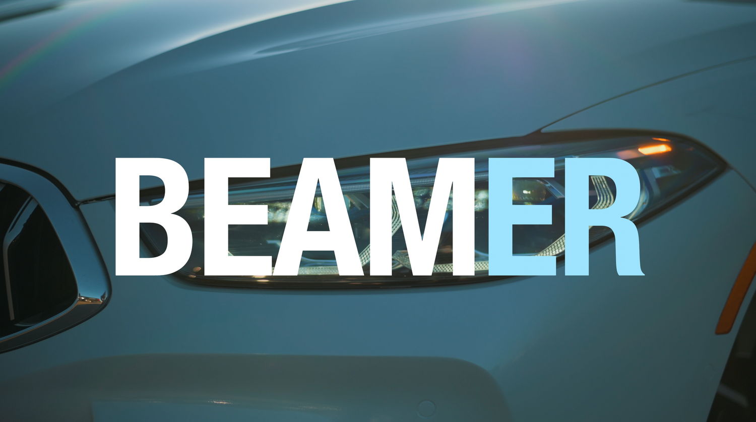 Close-up of a BMW headlight with bold BEAMER text overlay on a sleek blue luxury car.