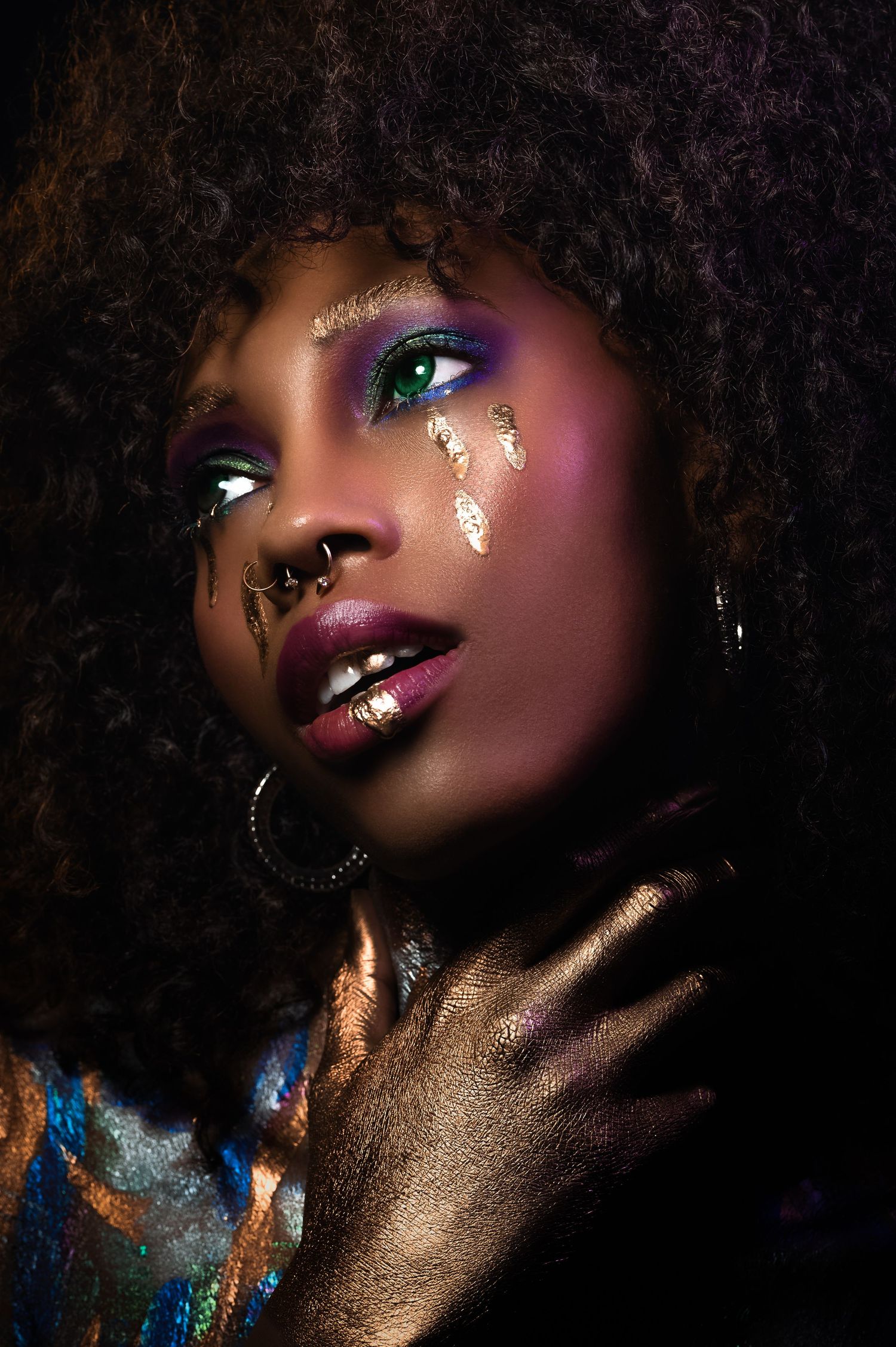 Artistic beauty portrait featuring dramatic gold glitter makeup and vibrant purple eyeshadow in a dark studio setting.