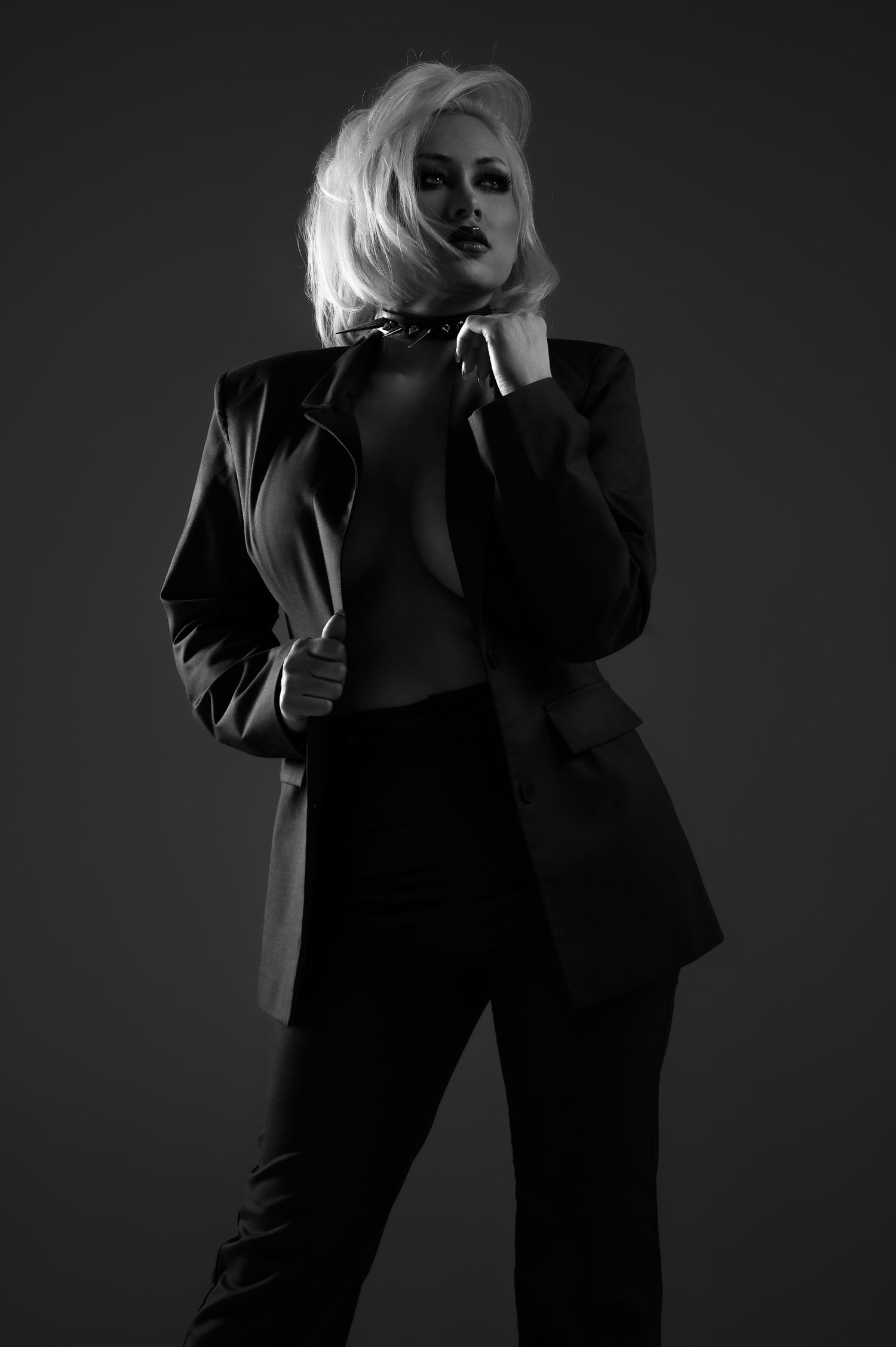 Black and white photo of a blonde woman in an oversized blazer and trousers, posing dramatically against a dark background.