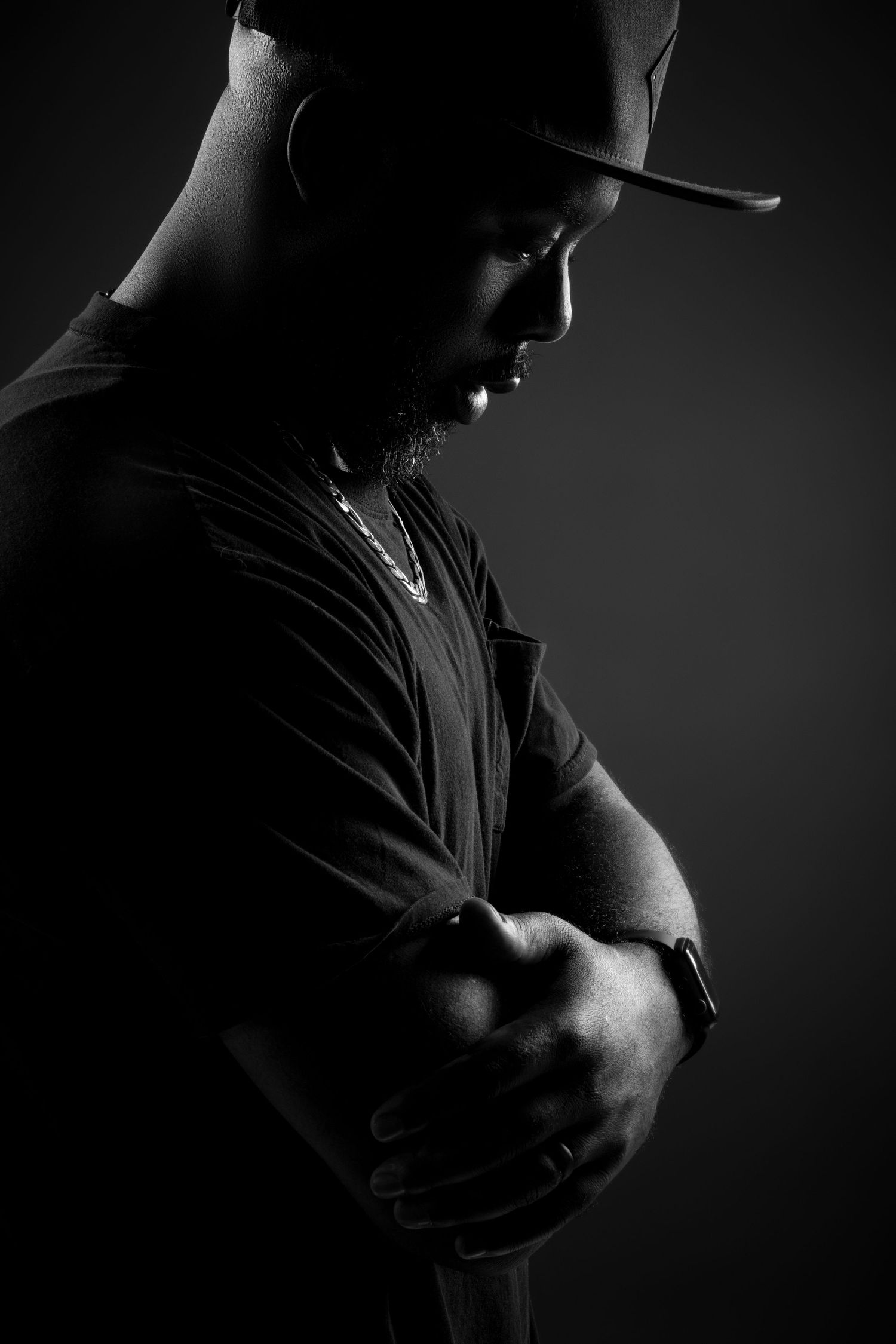 A dramatic black and white portrait silhouette of a person wearing a baseball cap in moody lighting.