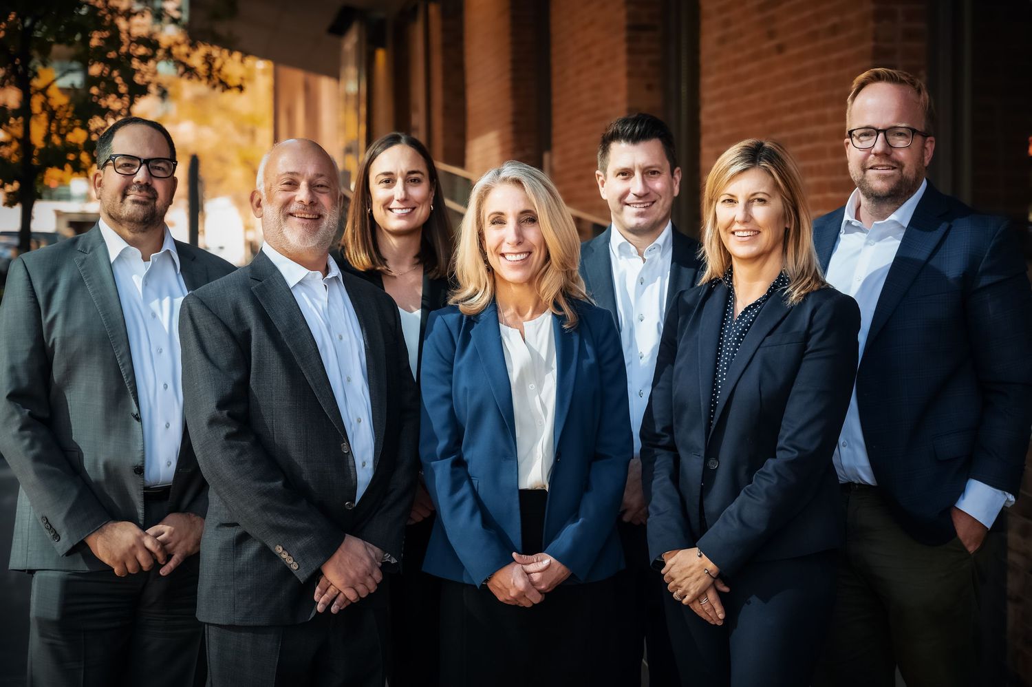 A group of business professionals in suits and formal attire stand together for a corporate team photo.