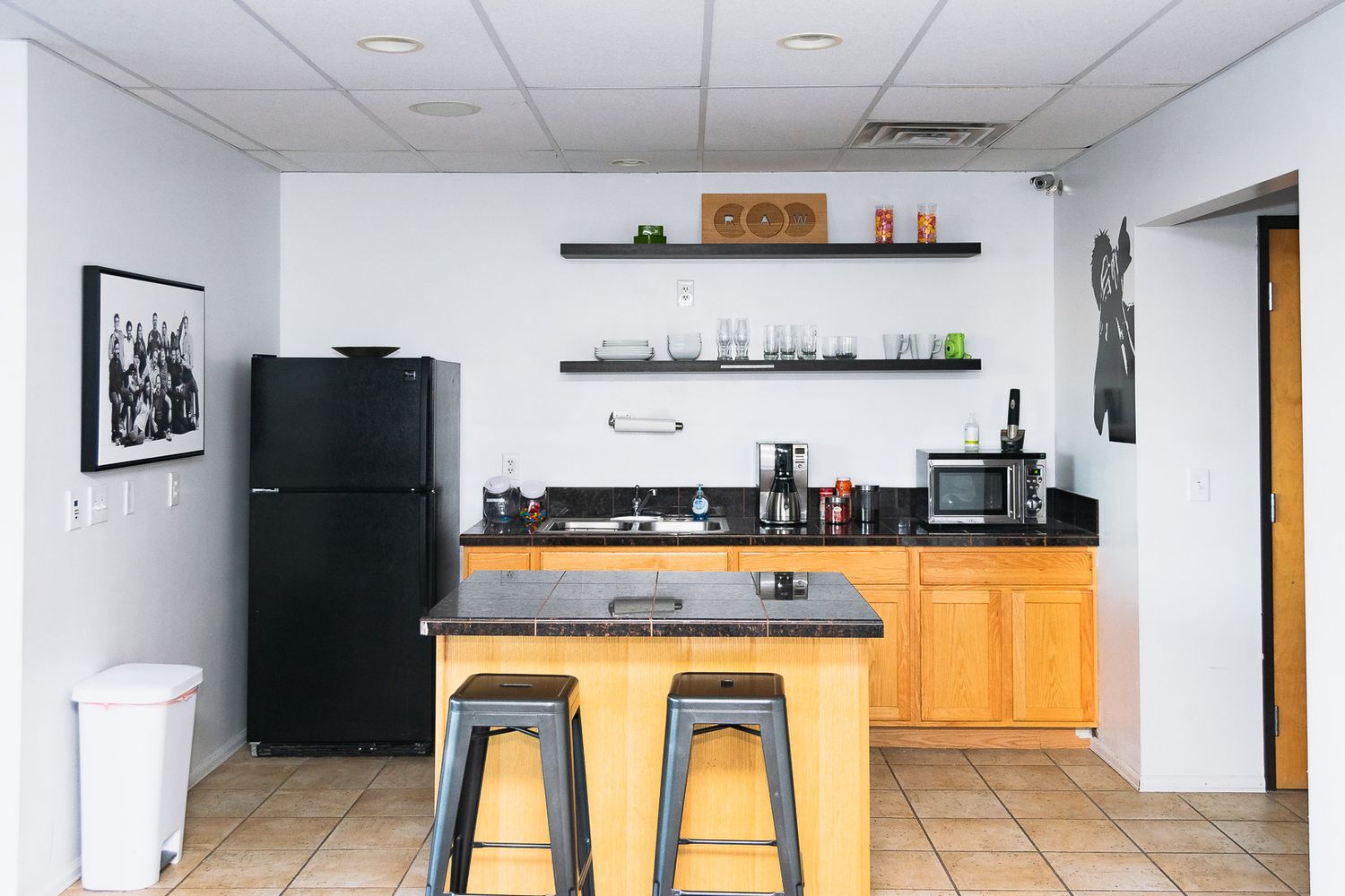 Modern kitchen with wooden cabinets, tile flooring, and bar stools at a white countertop peninsula.