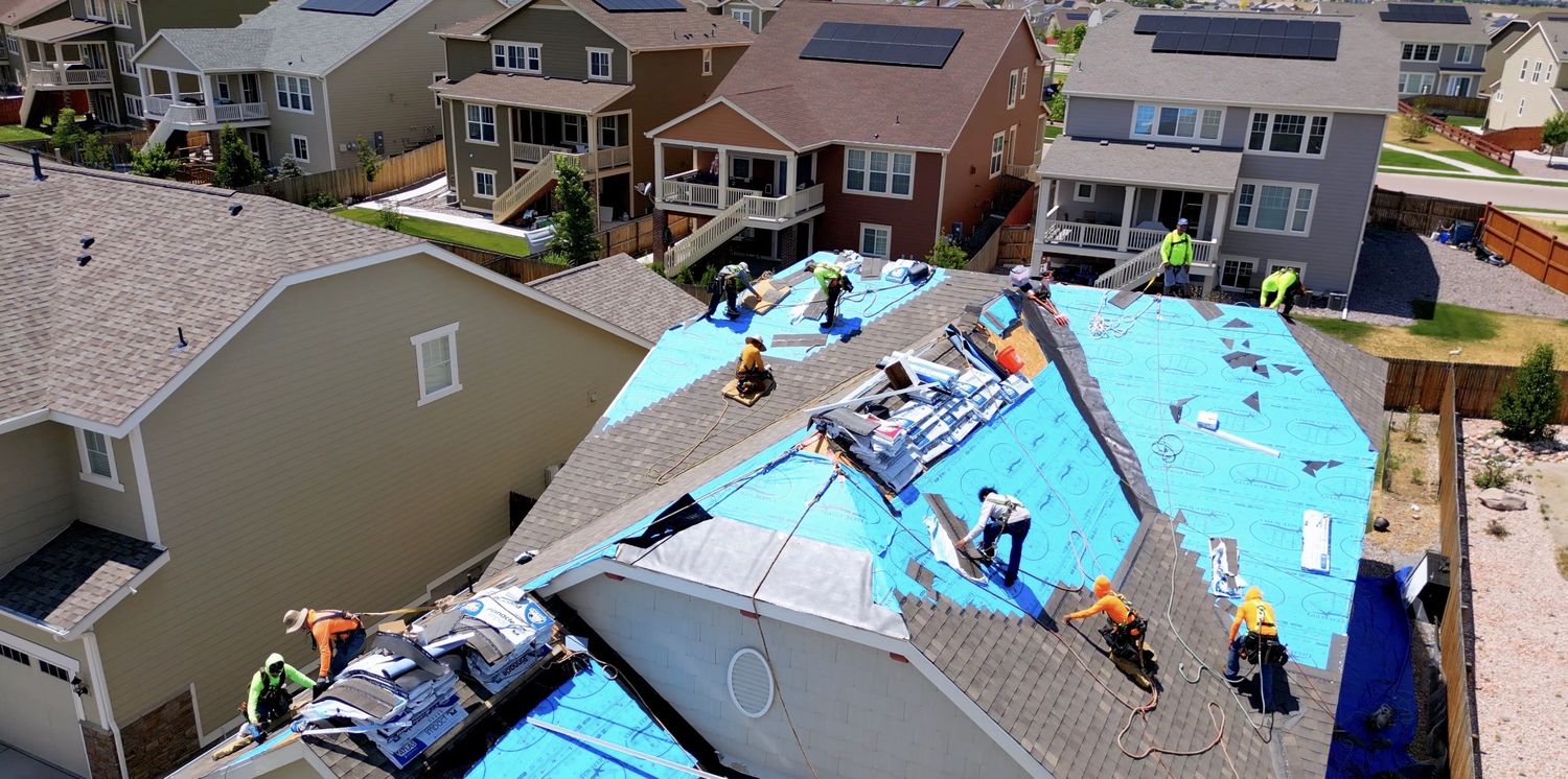 Aerial view of roofers installing blue underlayment on a residential house during construction or repair work.