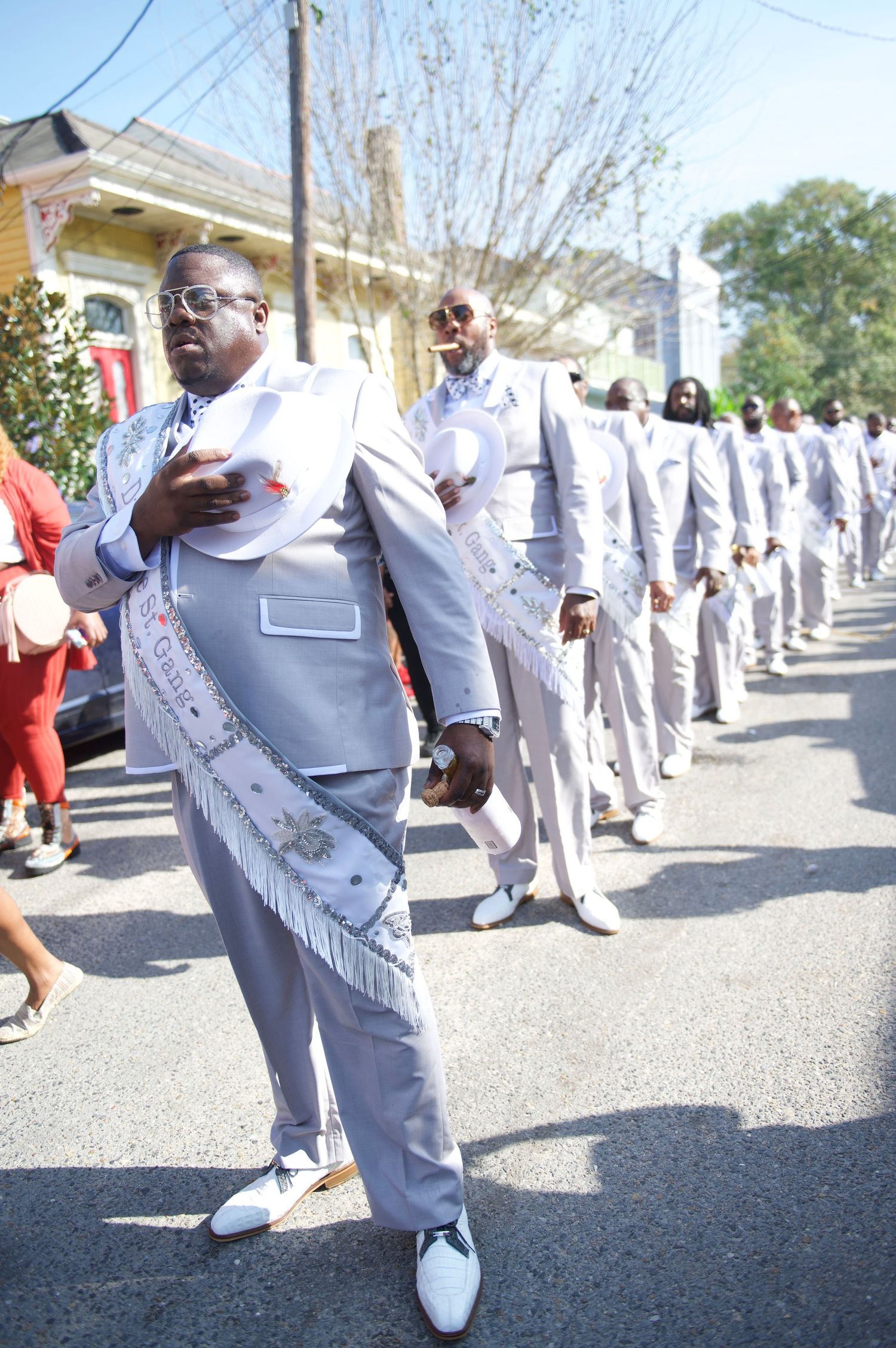 Line of dancers in matching light gray suits with silver trim performing in a street parade.