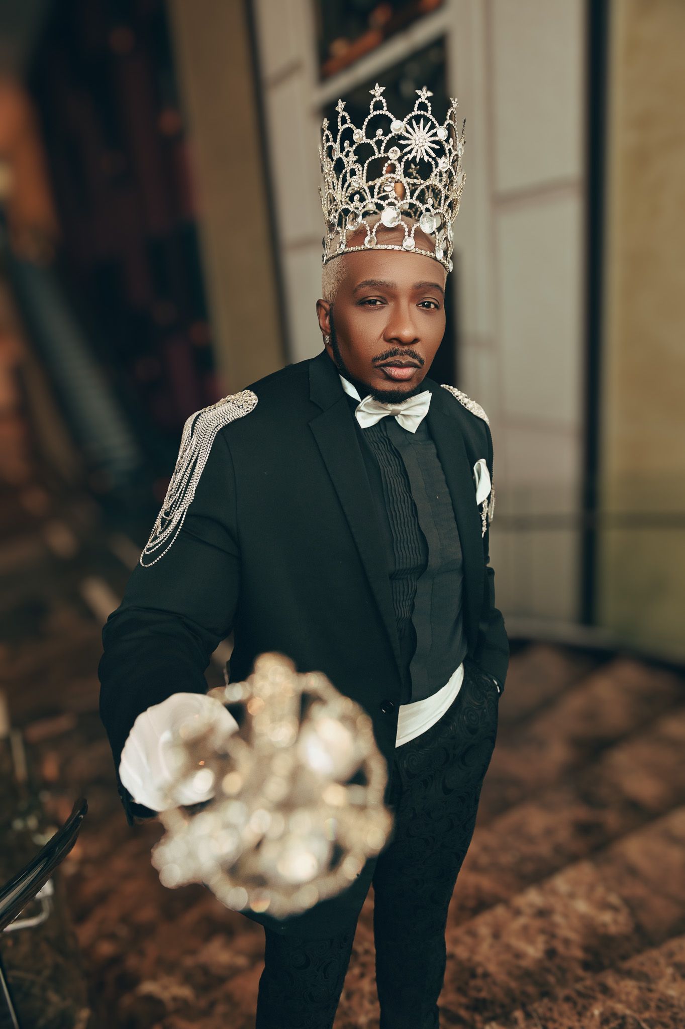 A formal portrait featuring a black tuxedo and crown against a dark background.