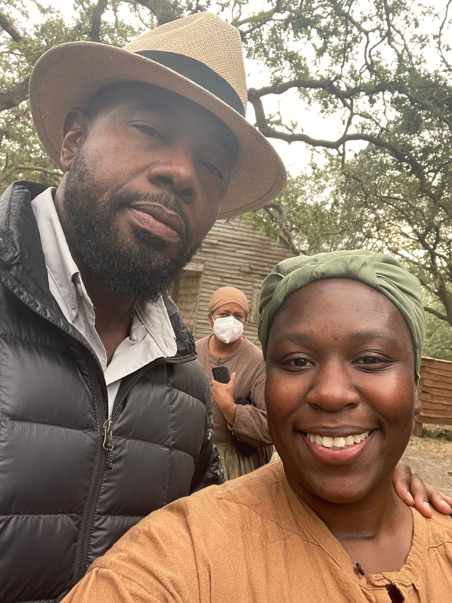 Two people take a selfie together outdoors under a tree.