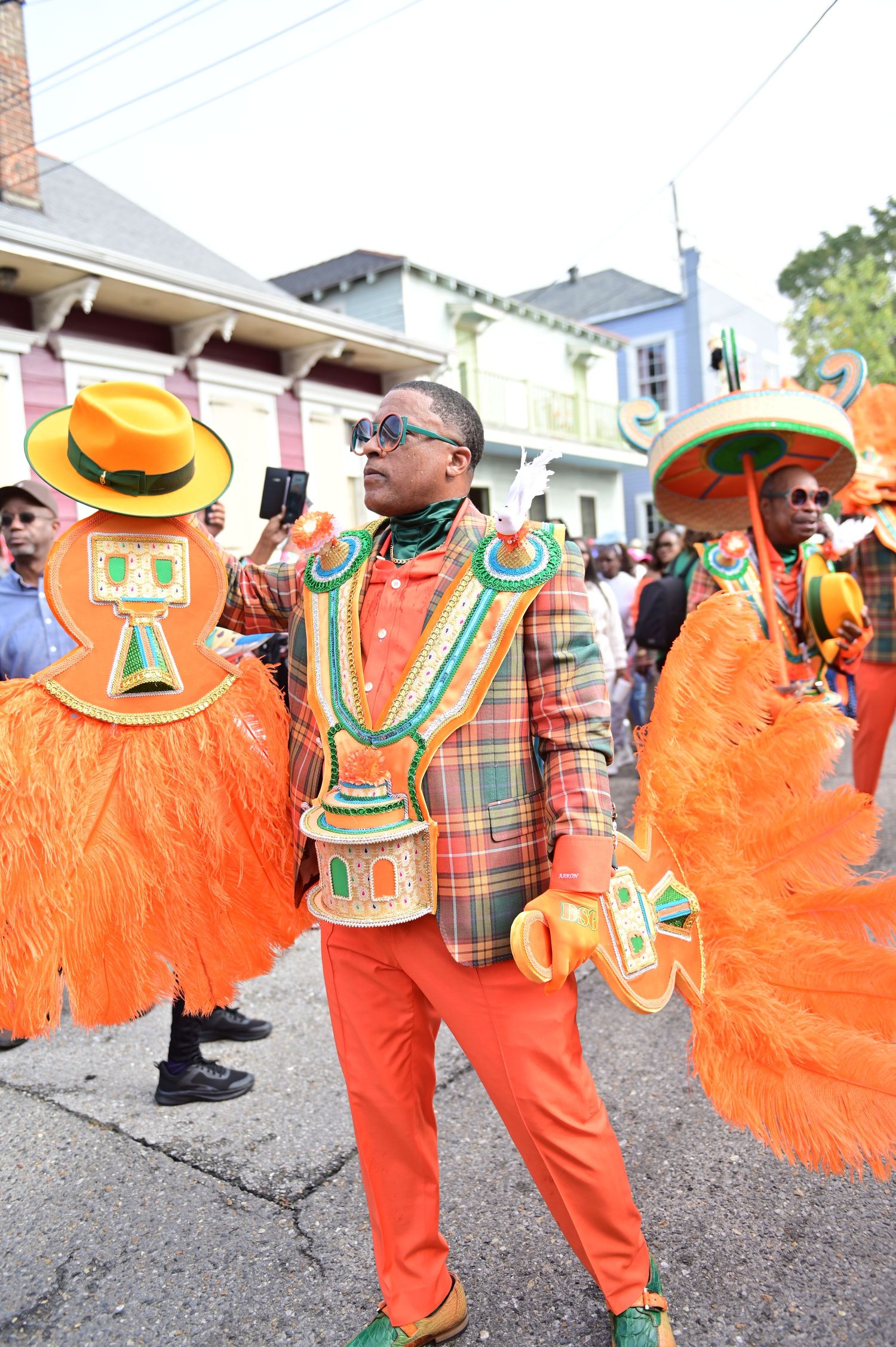 Street parade performers in bright orange costumes with decorative hats and plaid jackets.