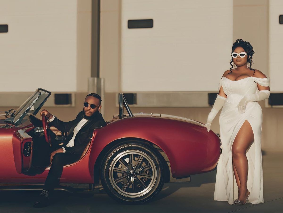 Vintage red sports car parked with elegantly dressed couple in formal attire.