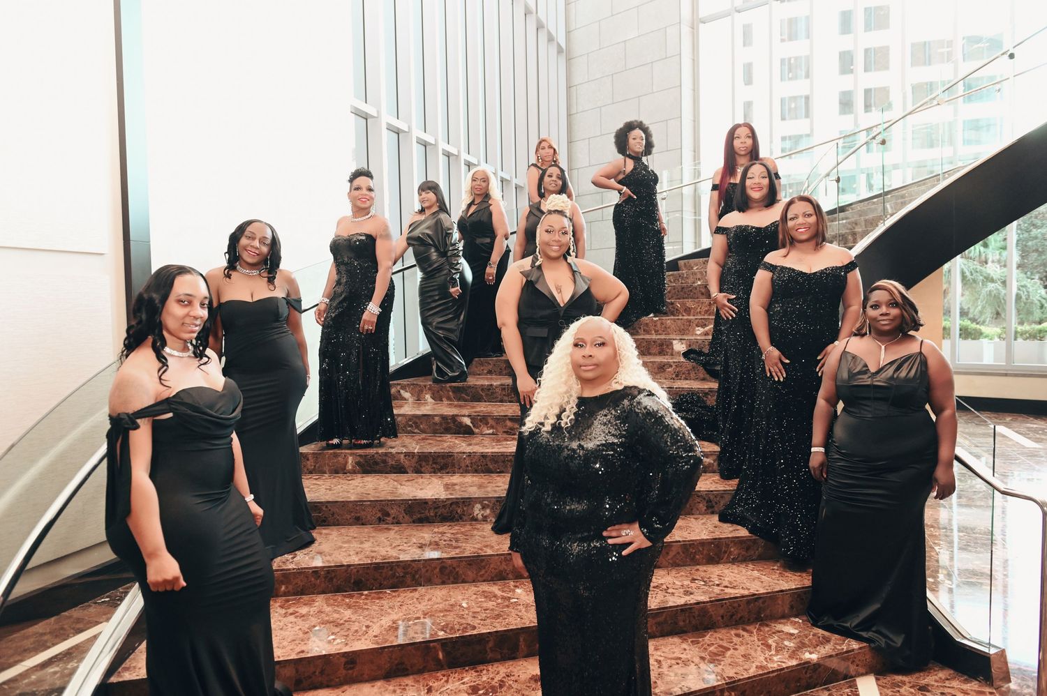 Group photo session with people in black dresses posing on brown marble steps.