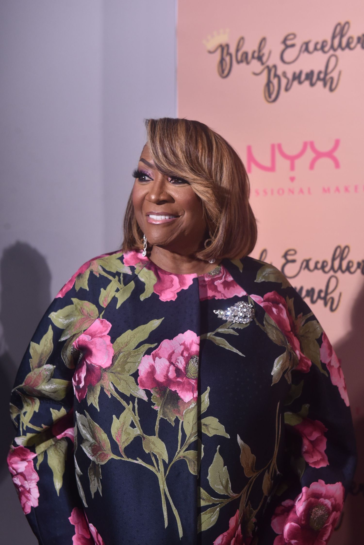 Woman in floral navy dress smiles at Black Excellence Brunch event with NYX Professional Makeup backdrop.