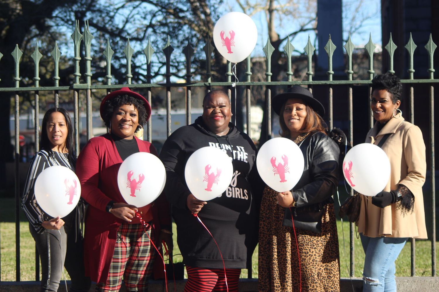 A group holding white balloons while standing against decorative iron fencing outdoors.