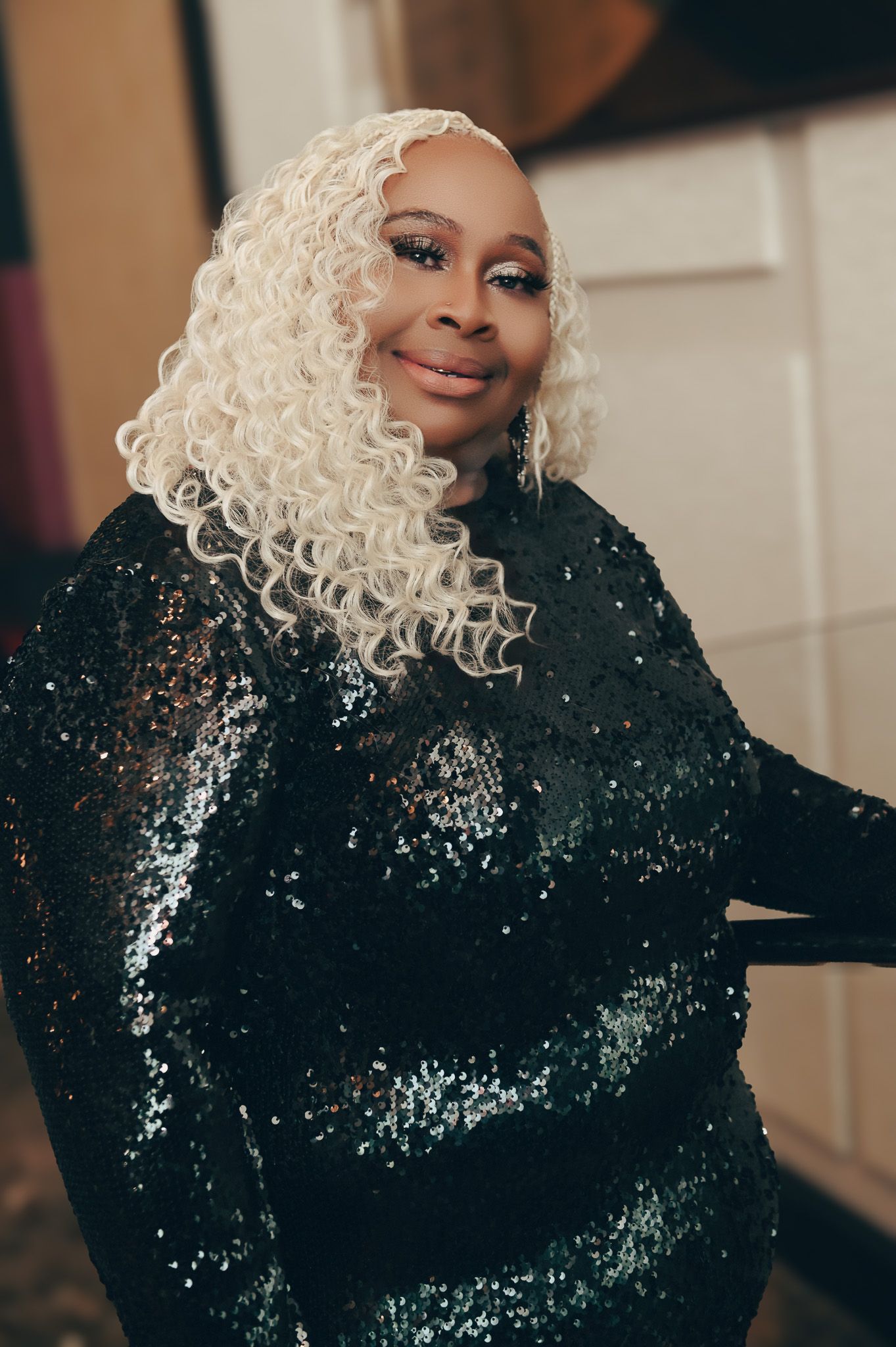 A stunning black sequin gown is paired with platinum blonde curls in a glamorous portrait.