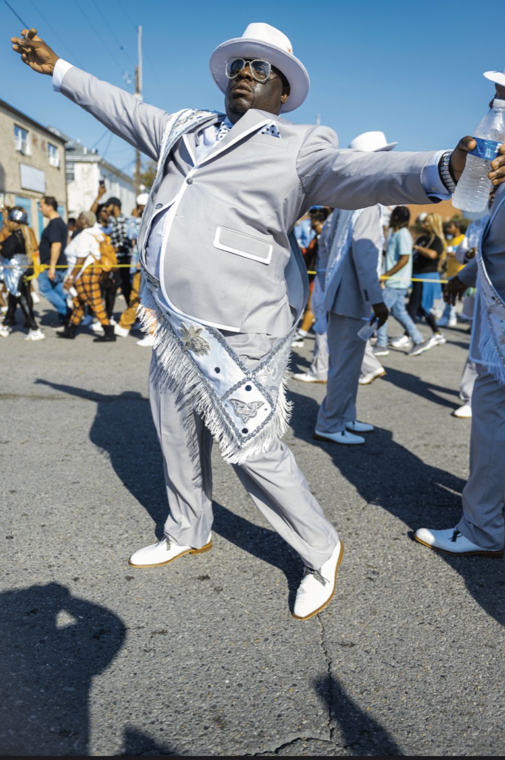 Street dancers in white outfits perform energetic breakdance moves on pavement during an outdoor event.