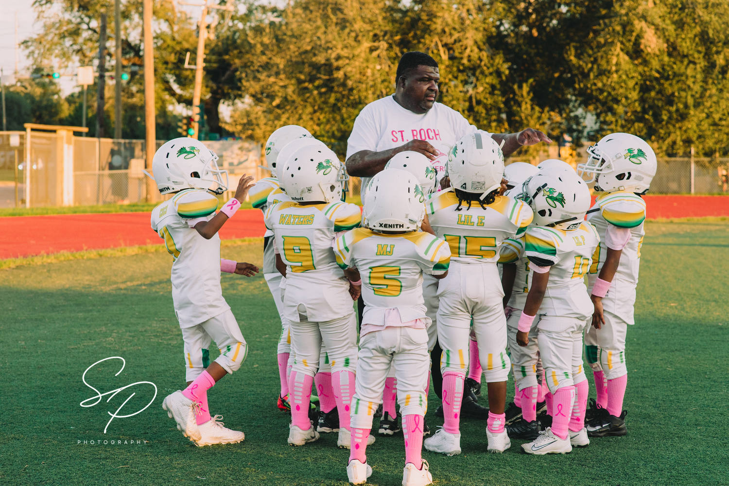 Football players huddle together on a sunny field wearing white uniforms with pink socks.