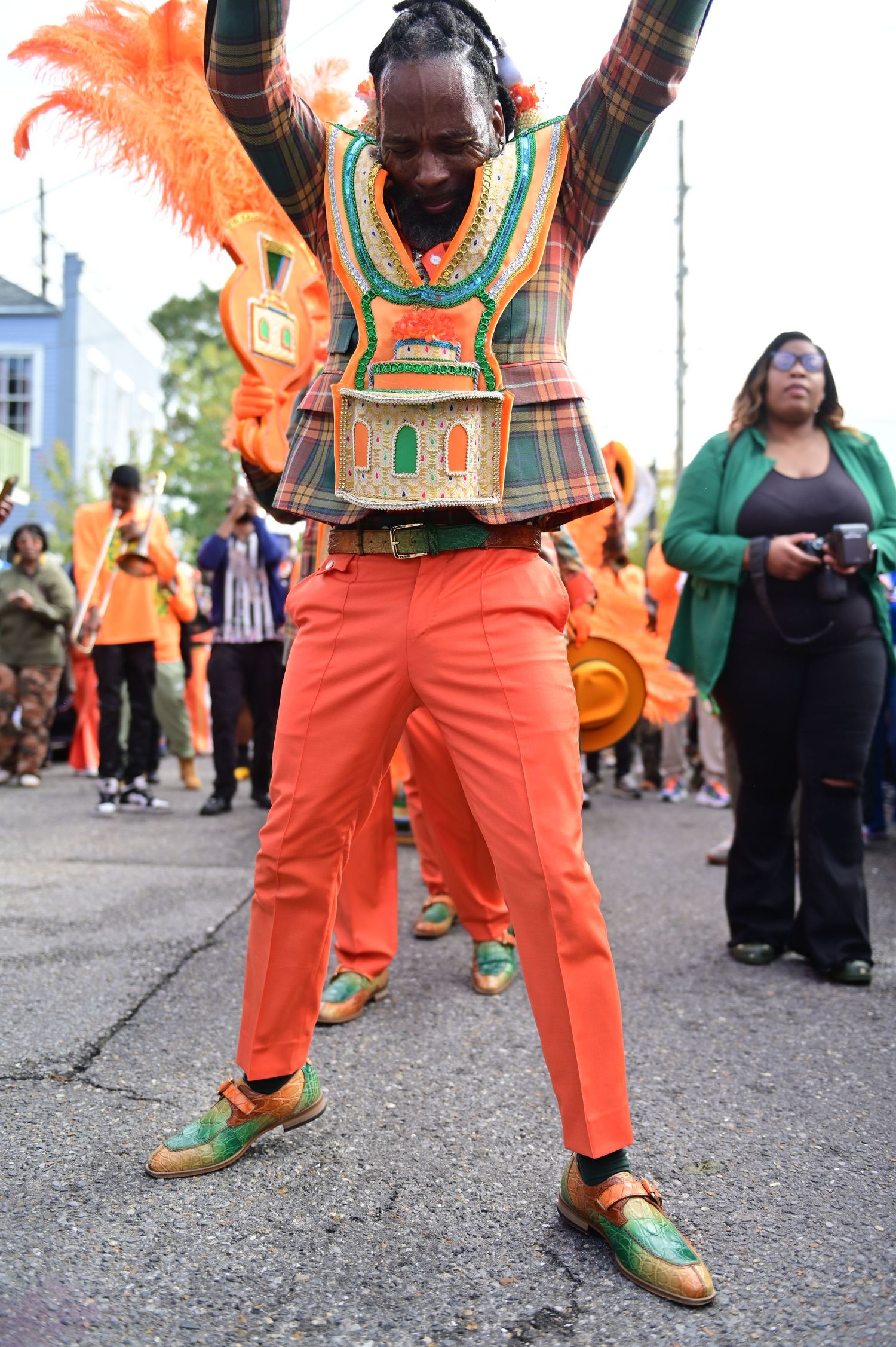 Dancer in colorful plaid vest and orange pants performs energetic move at outdoor event.