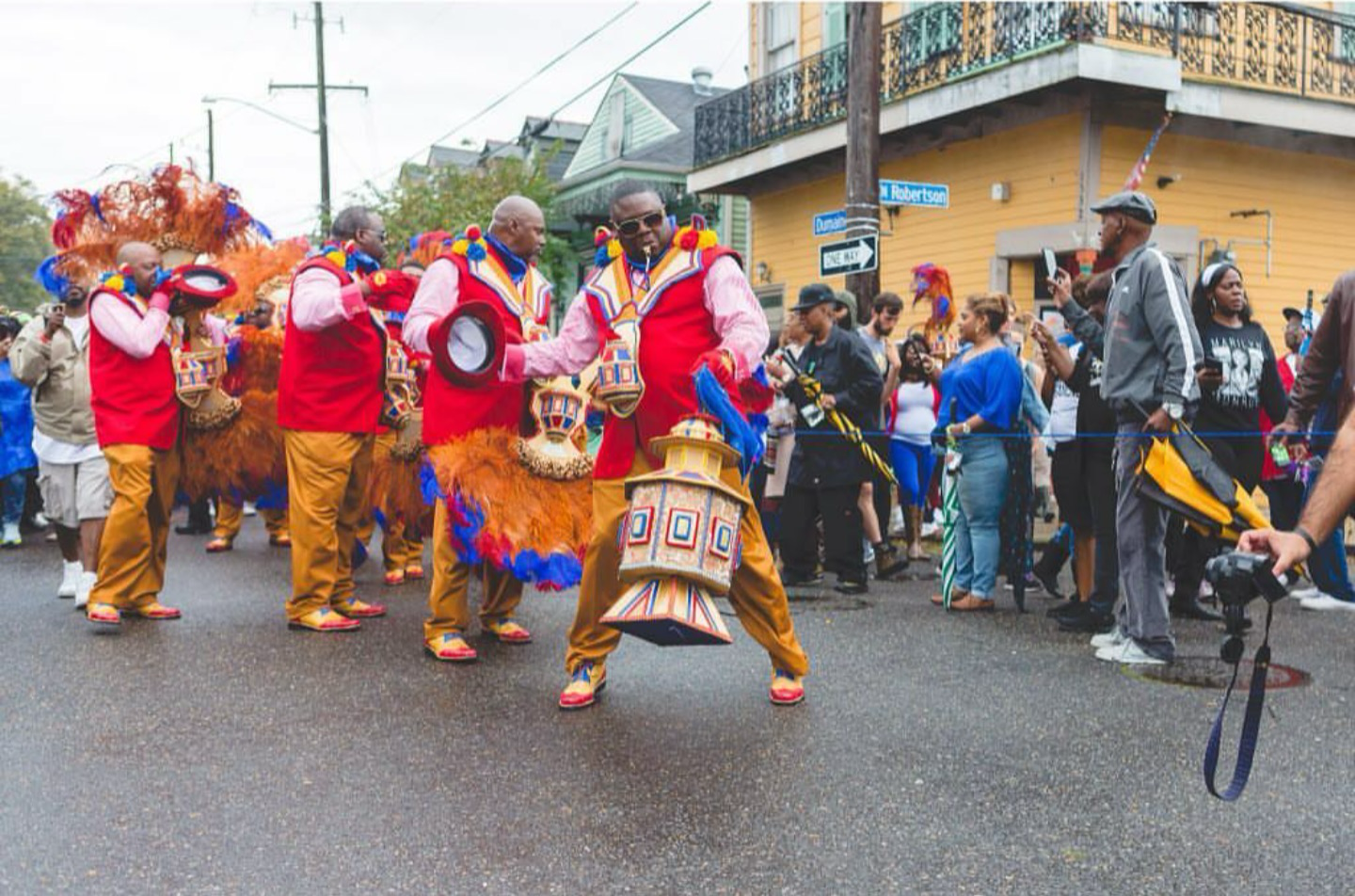 Costumed performers in brown animal outfits dance in a street parade while spectators watch from the sidelines.