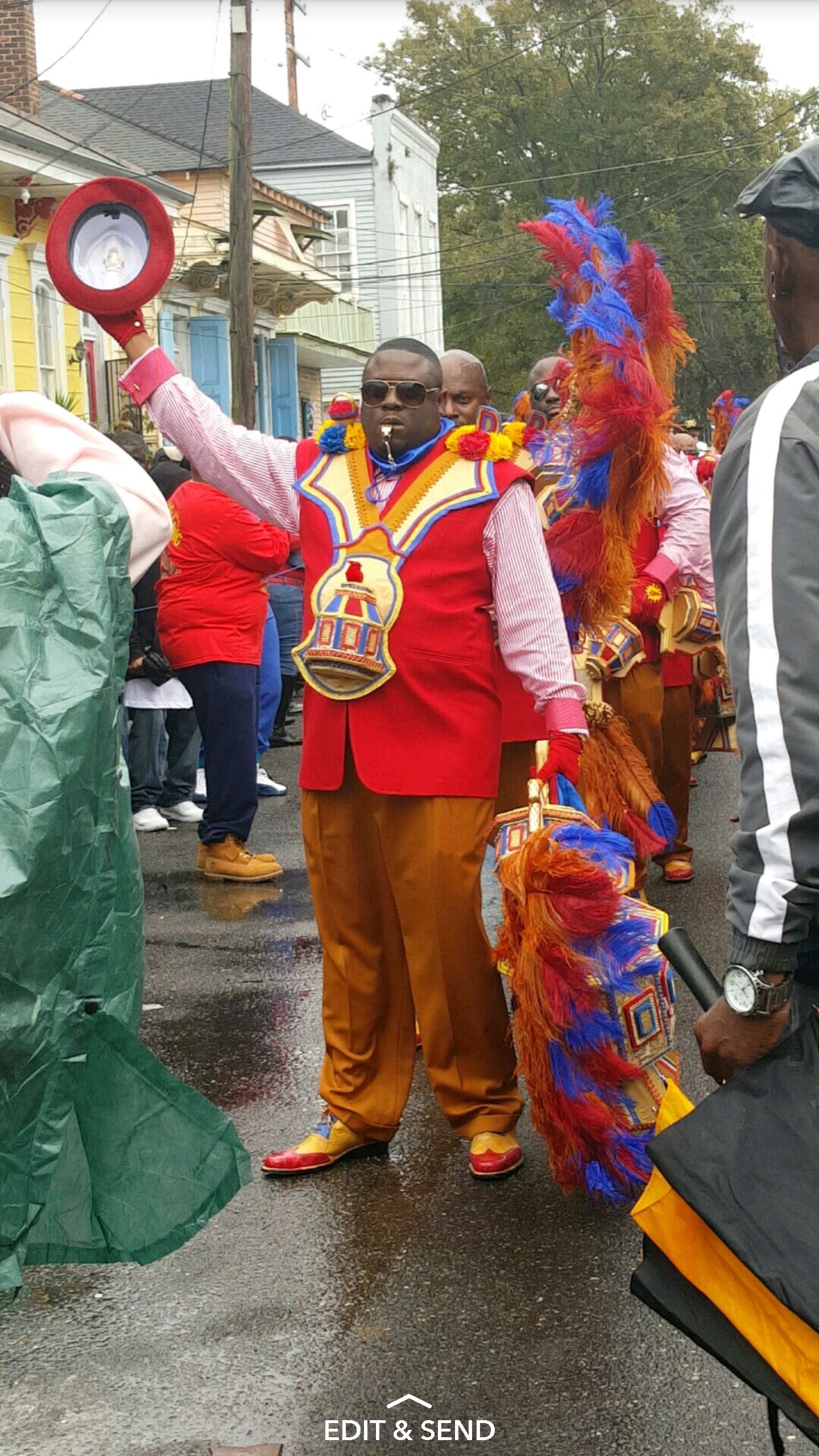 Festive parade participants wearing bright red and orange costumes with feathered headdresses on a rainy street.