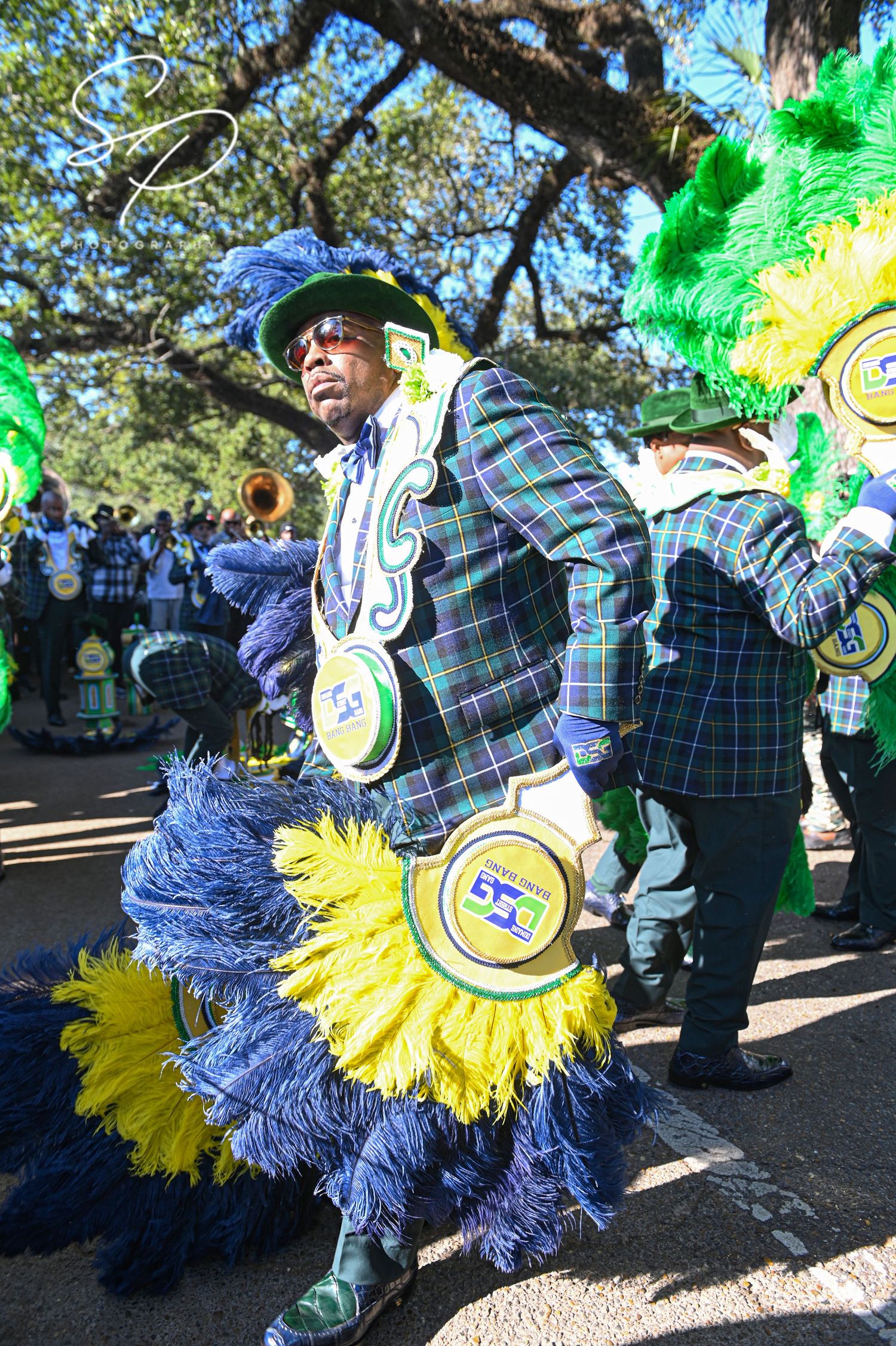 Dancers wearing plaid uniforms with blue and yellow feathers performing at an outdoor event.