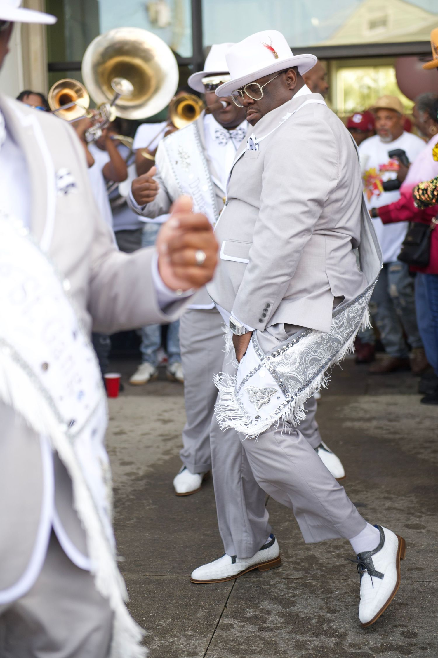 Second line dancer in white suit and hat performing traditional New Orleans dance moves.