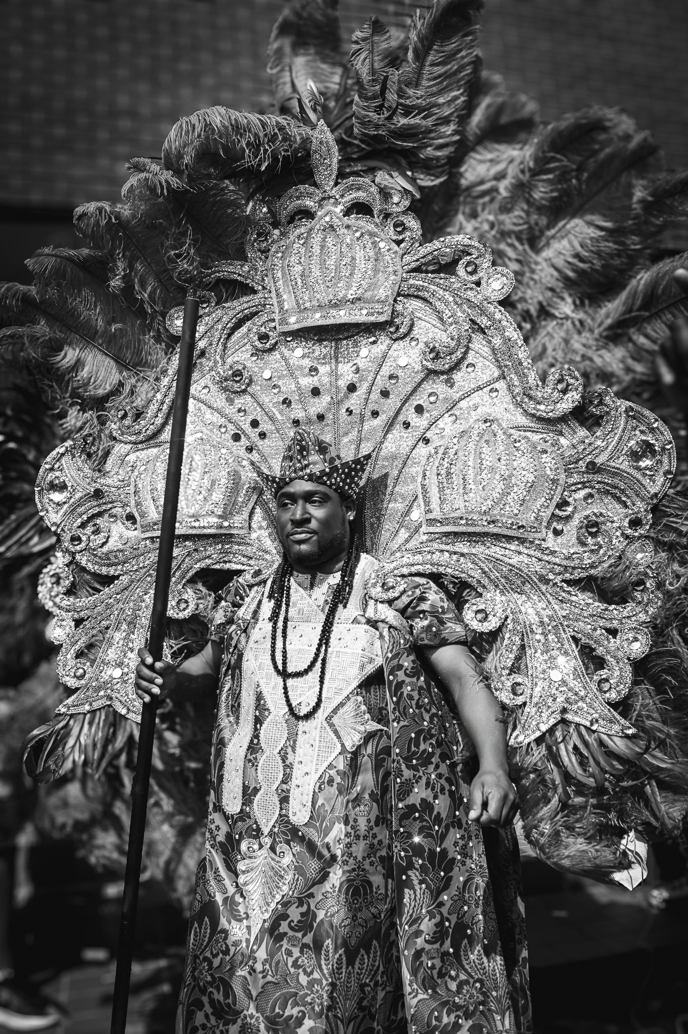A black and white photo series of a carnival performer wearing an elaborate feathered headdress and costume.