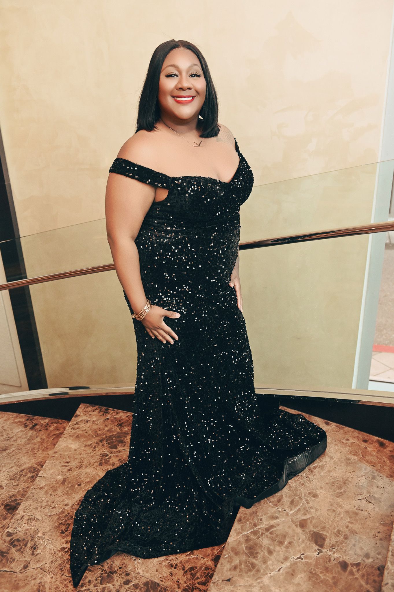 Person in sparkly black evening gown poses elegantly on marble floor.