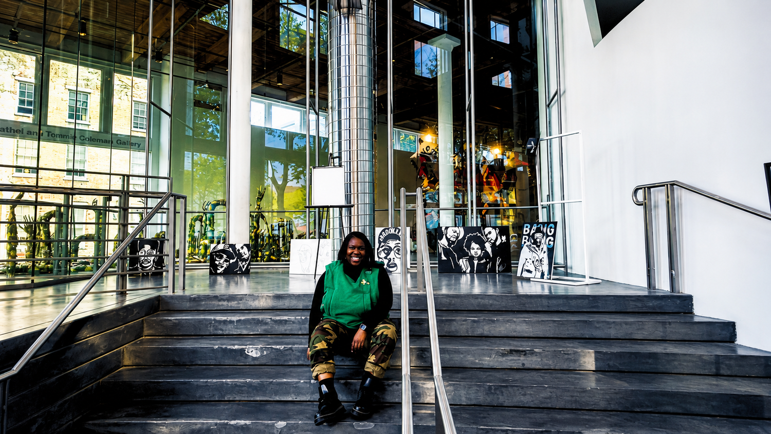 Person sitting on steps outside a modern glass building entrance with decorative sculptures in the background.
