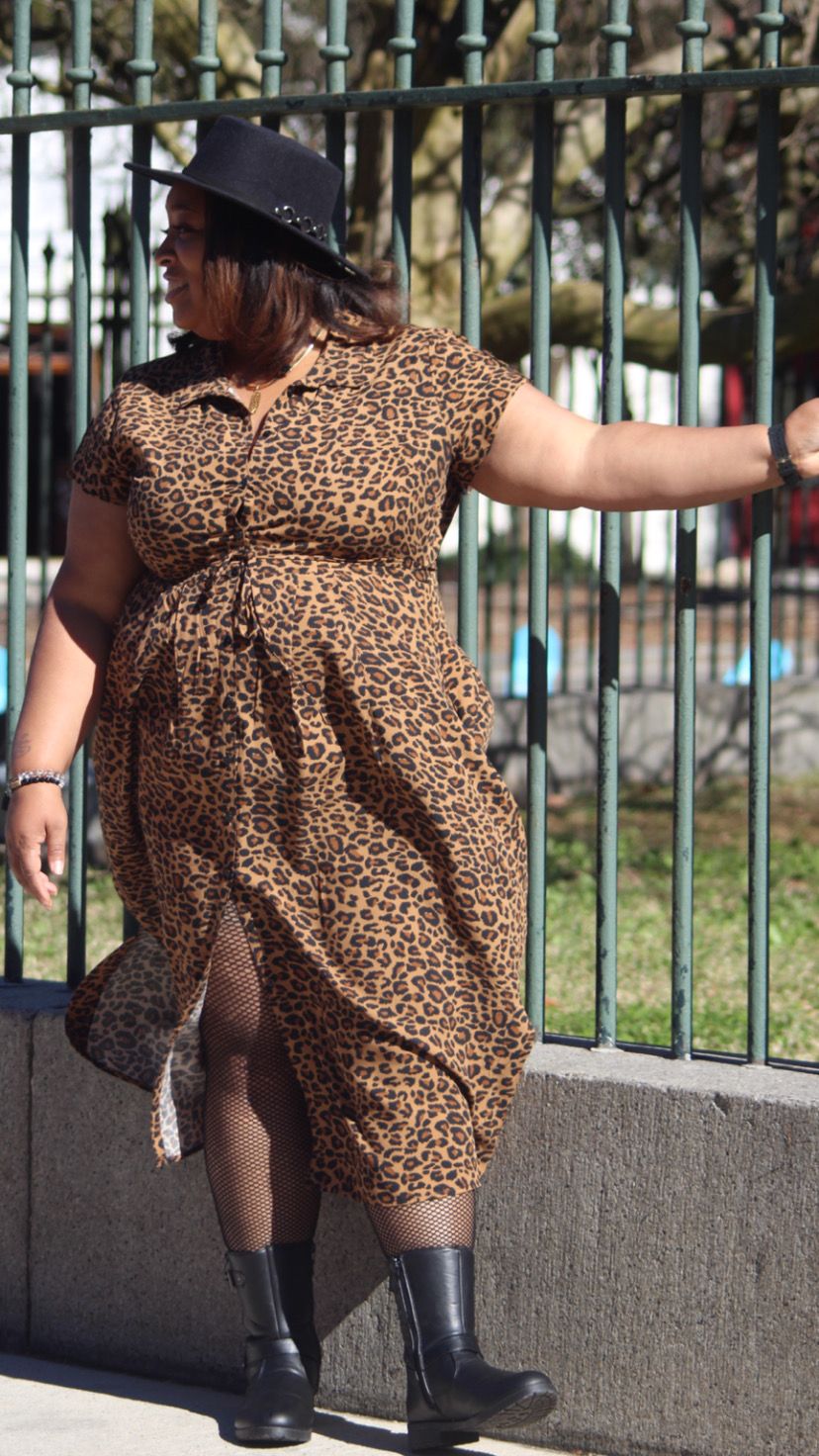 Child in leopard print dress and boots playing near metal fence.
