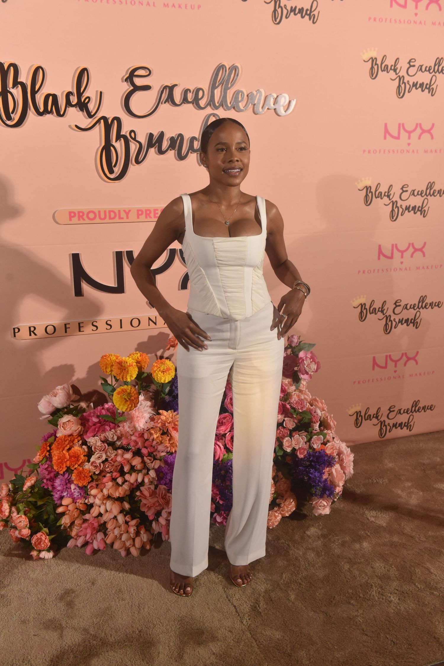 Woman in white jumpsuit posing at Black Excellence Brunch event sponsored by NYX Professional Makeup.