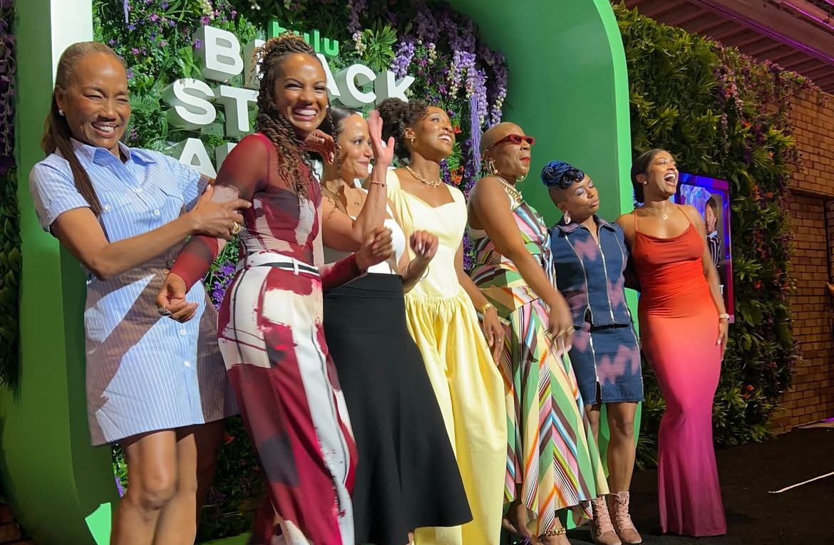 Group photo under green arch at social event with decorative wall backdrop.