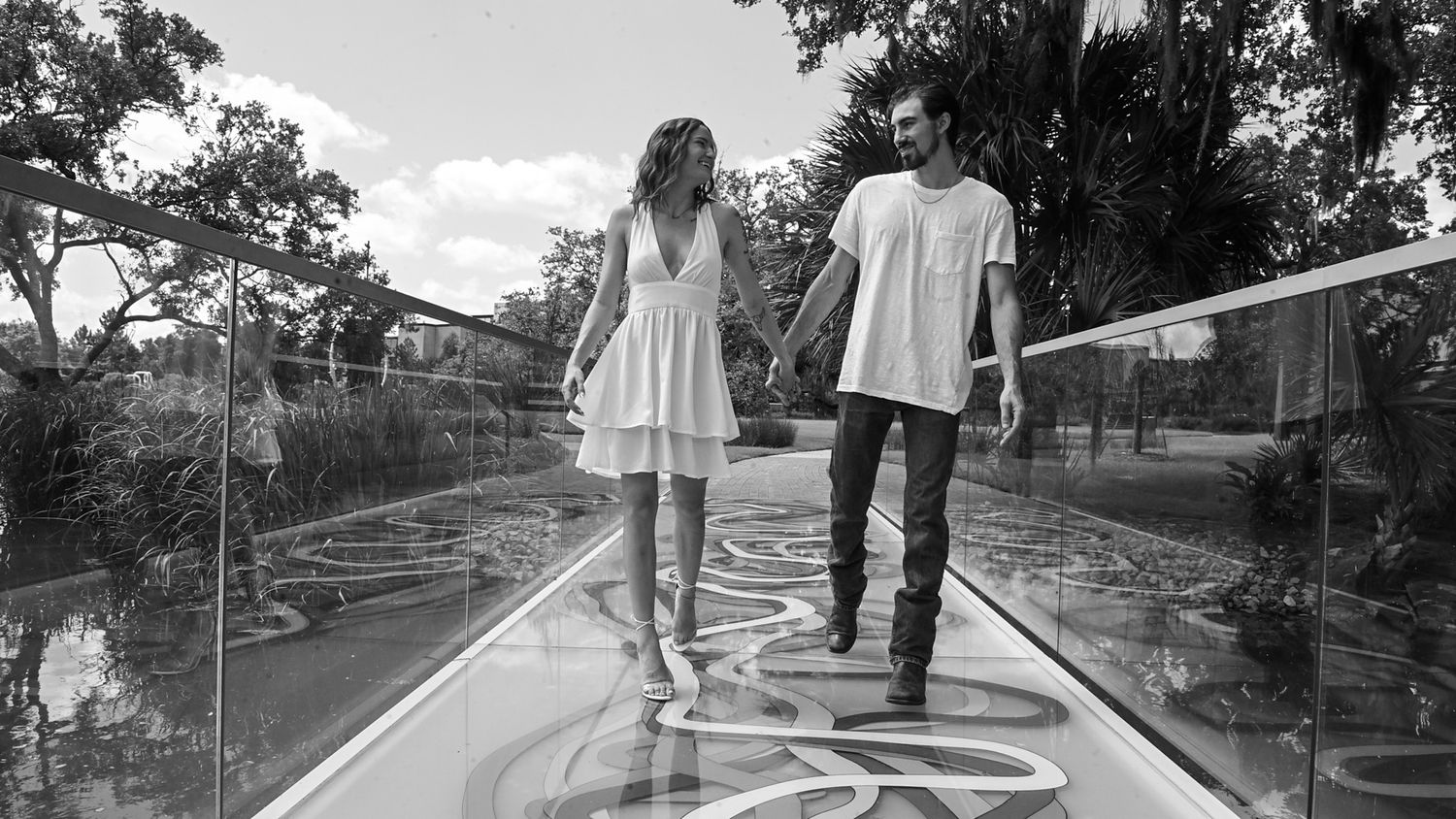Couple walking together on elevated wooden boardwalk in black and white.