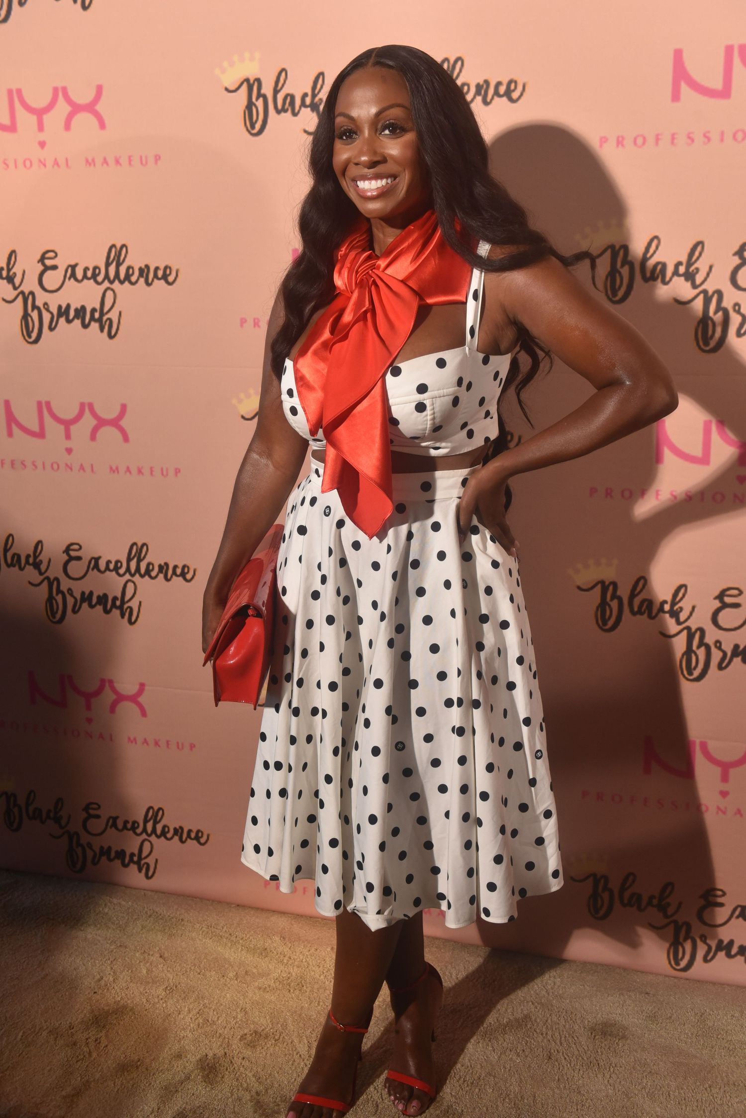 Woman in polka dot dress with red bow poses at NYX Professional Makeup Black Excellence Brunch.