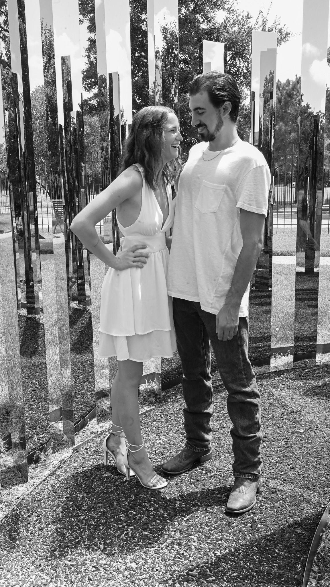 Couple poses playfully between mirrored columns in outdoor art installation.
