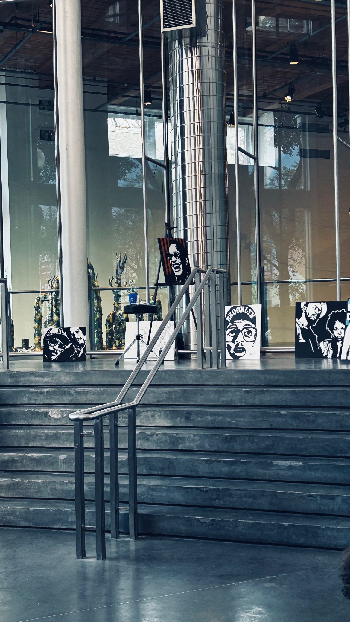 Modern building interior with glass walls and concrete steps featuring black and white portrait artwork displays.