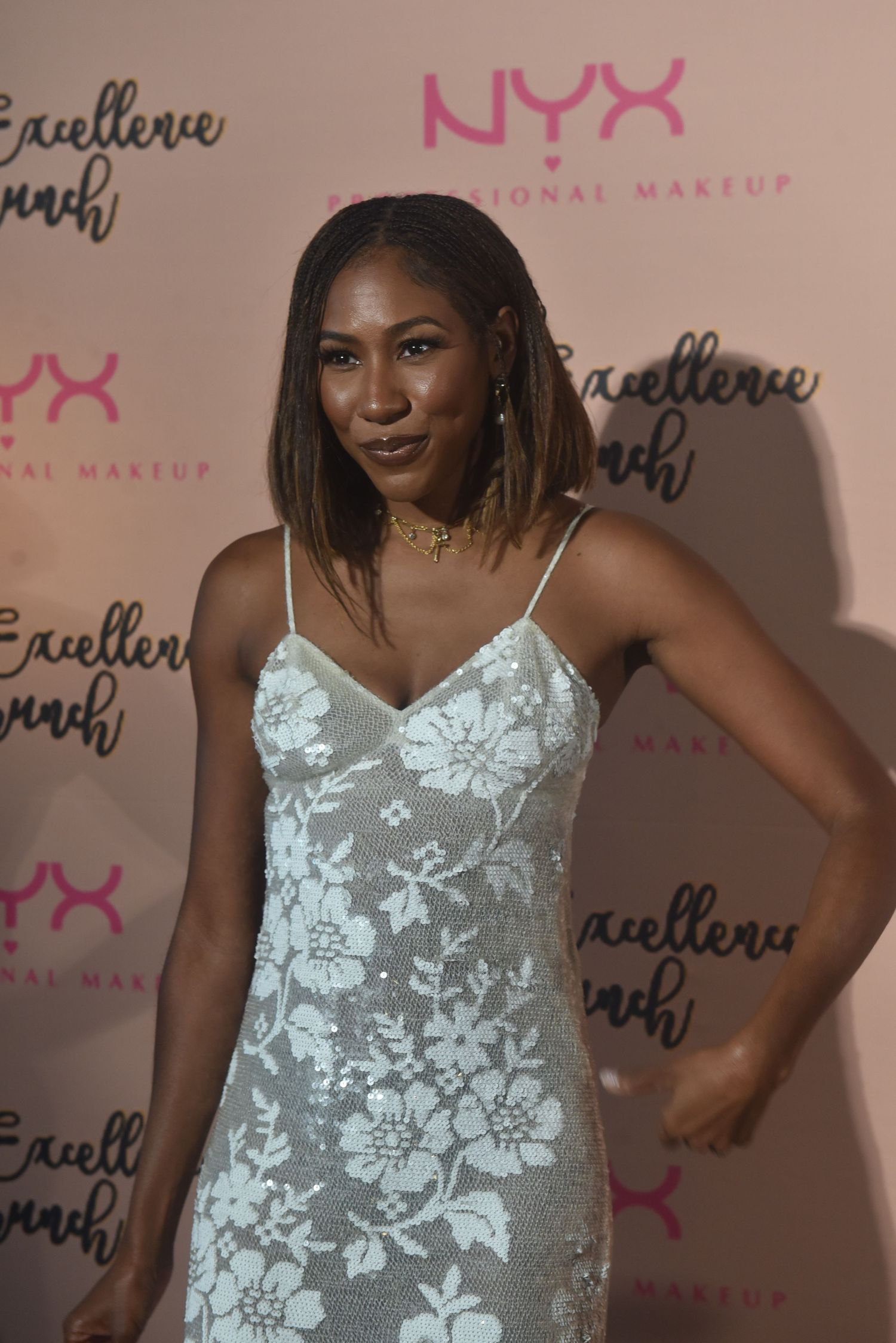 Woman in white floral dress poses at NYX Professional Makeup Black Excellence Brunch event.