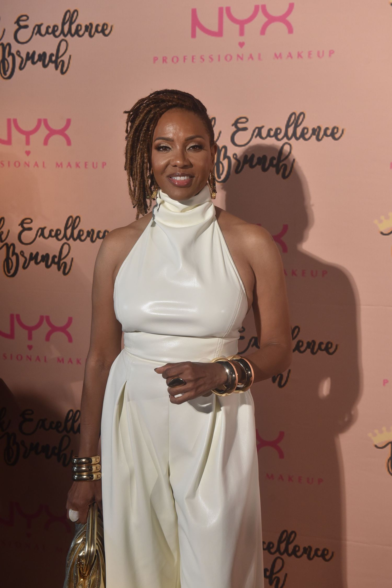 Woman in white halter jumpsuit poses at NYX Professional Makeup Black Excellence Brunch event.