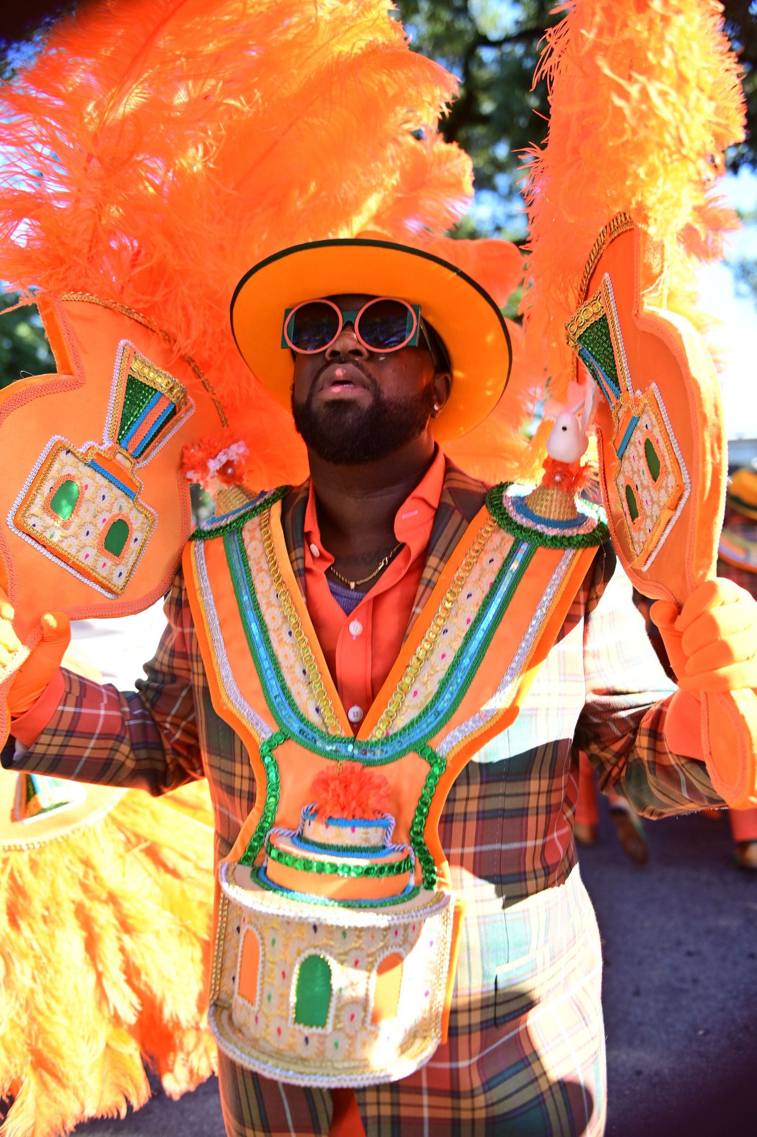 Performer wearing ornate plaid costume with orange feathers dances during festival.