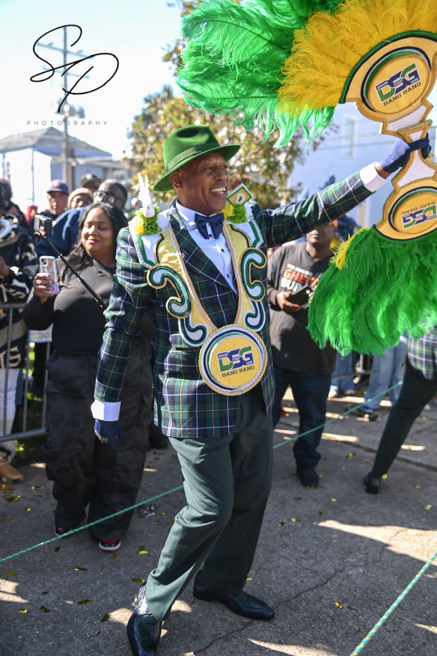 Street dancers in green and yellow feathered costumes performing synchronized movements.