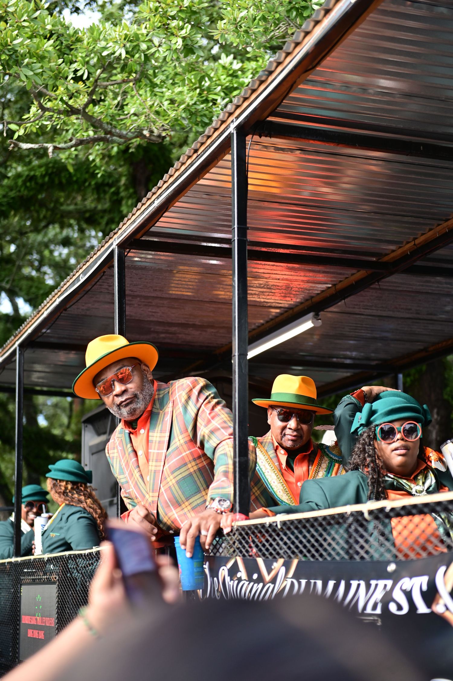 Performers in bright outfits and hats entertain crowd from elevated stage platform.